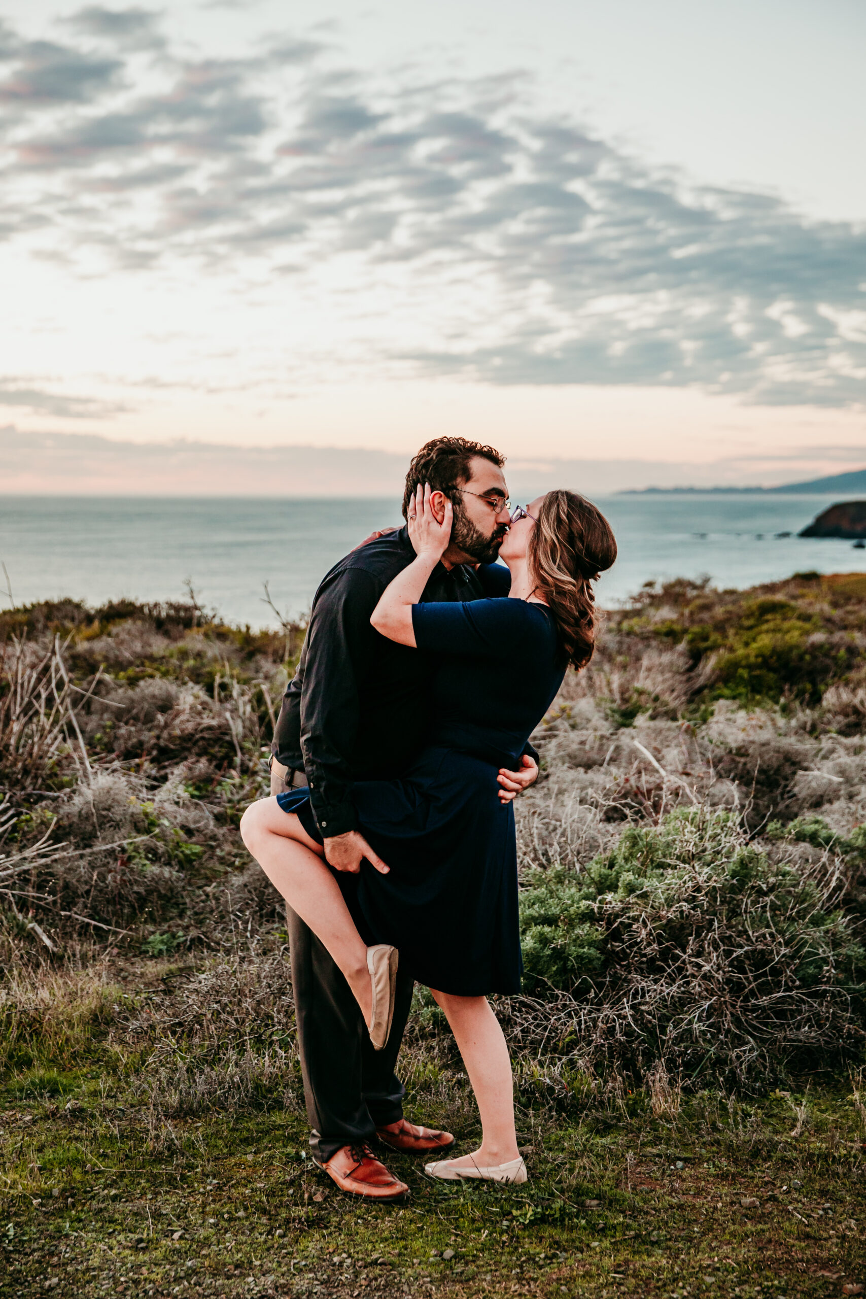 Couple sharing a passionate kiss on the coastal cliffs at sunset, captured by San Francisco engagement photographer Kristin Smith.