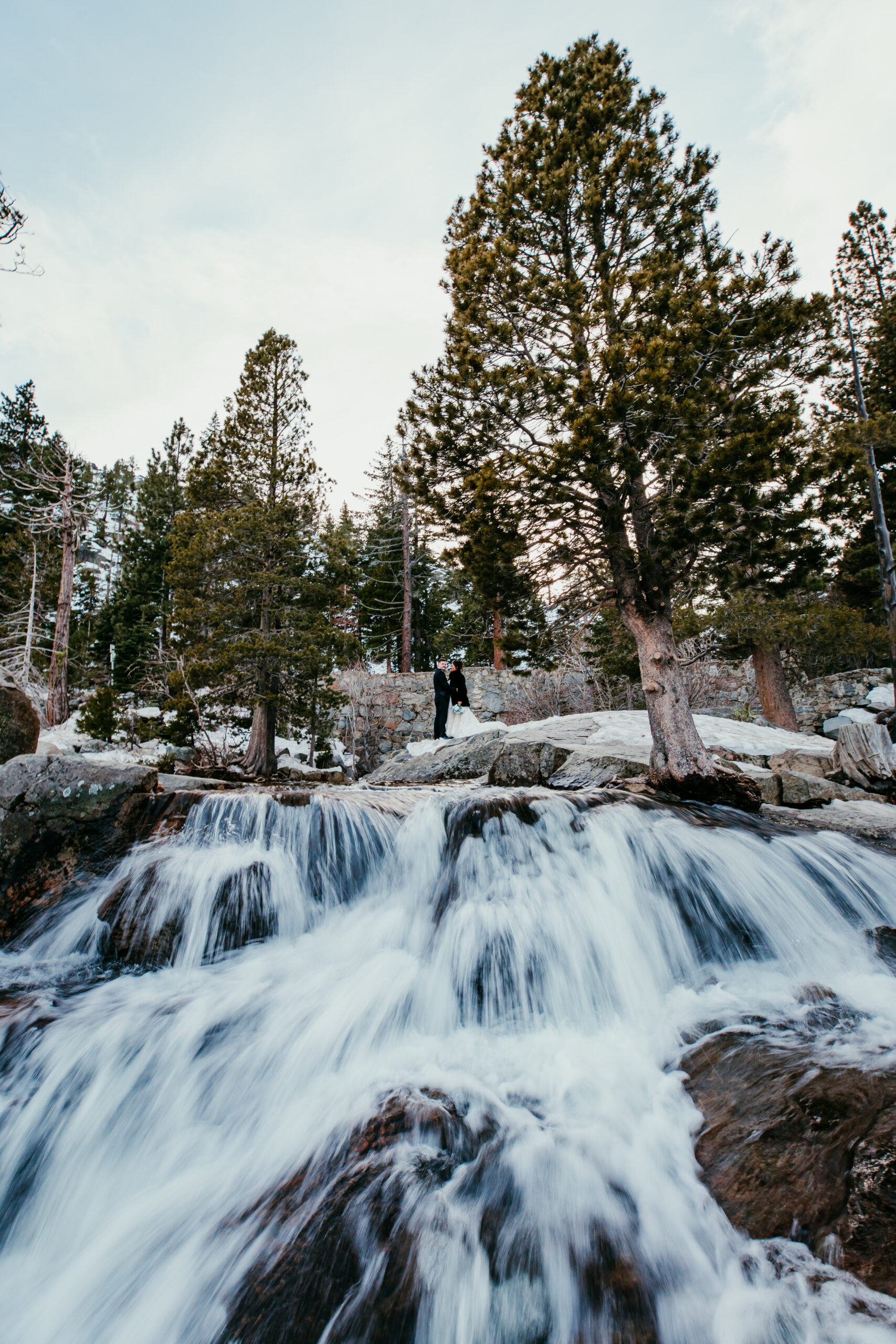 Couple standing above a waterfall during a mountain elopement, representing the freedom couples seek when researching what states allow self-solemnization.