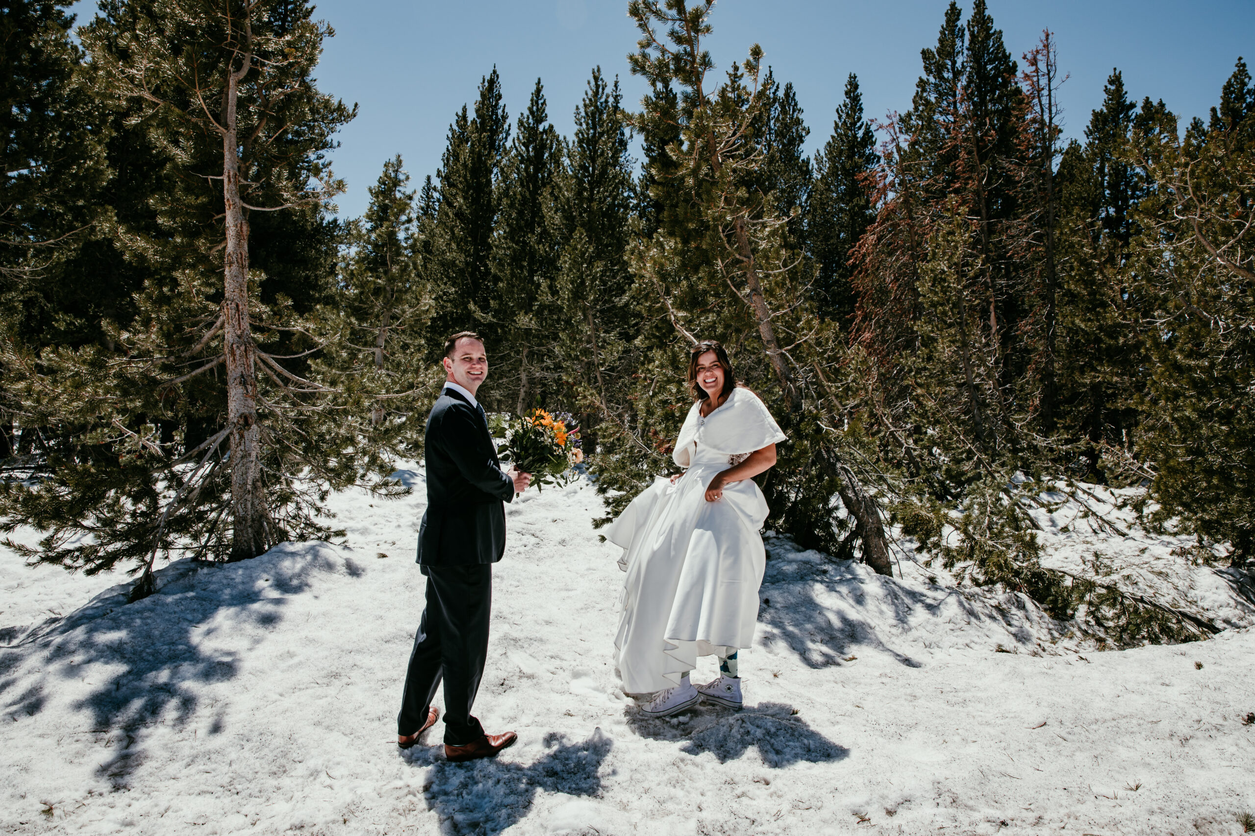 Bride and groom smiling in the snow during their Lake Tahoe fall elopement, surrounded by evergreens and bright mountain light.