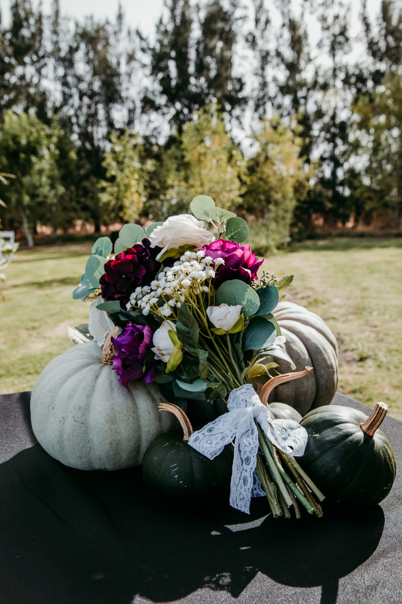 Moody fall bridal bouquet with deep purple, white, and green florals resting on pumpkins at a backyard wedding in Vacaville, CA