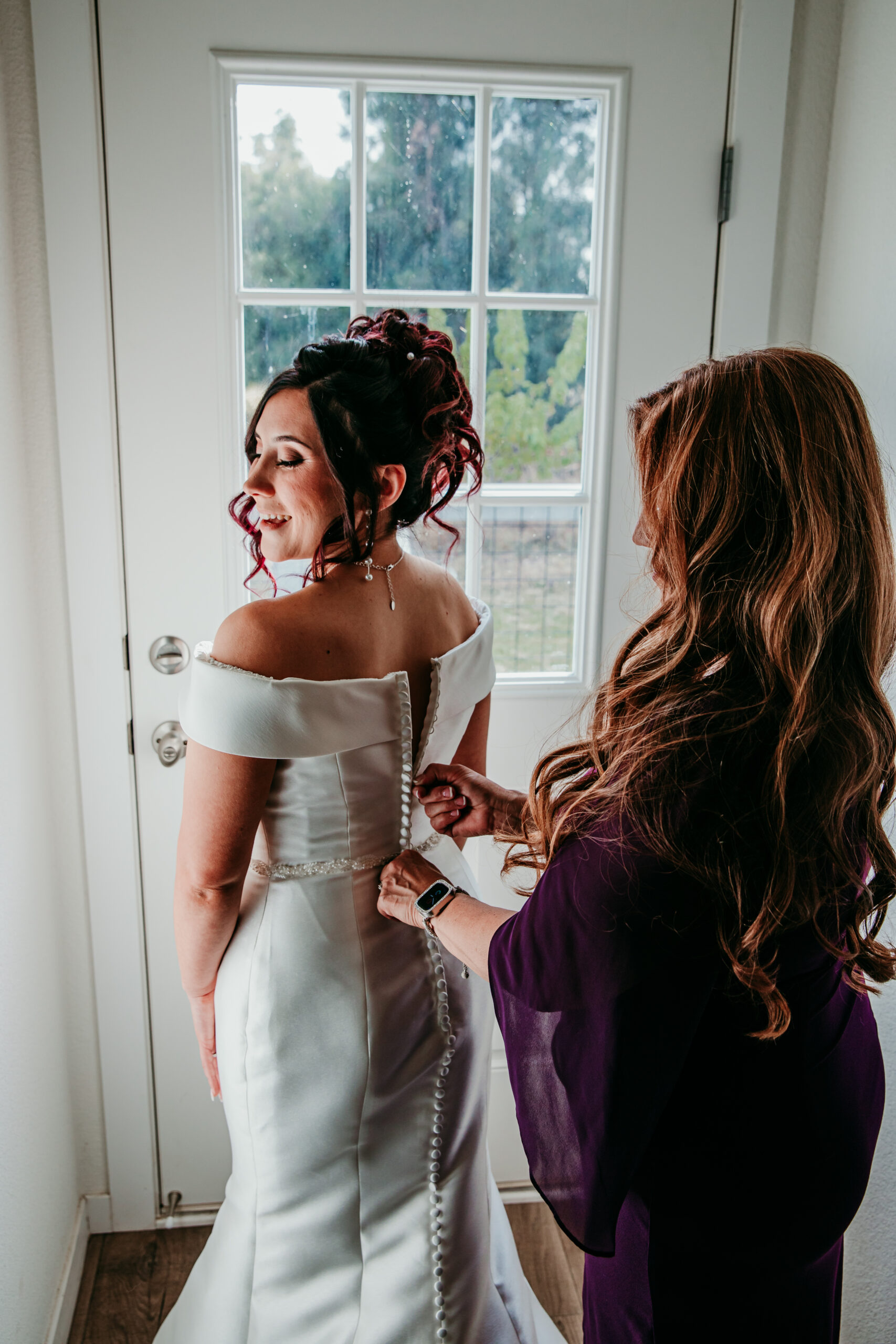 Bride getting buttoned into her off-the-shoulder wedding gown by her mother before a backyard fall wedding in Vacaville, CA