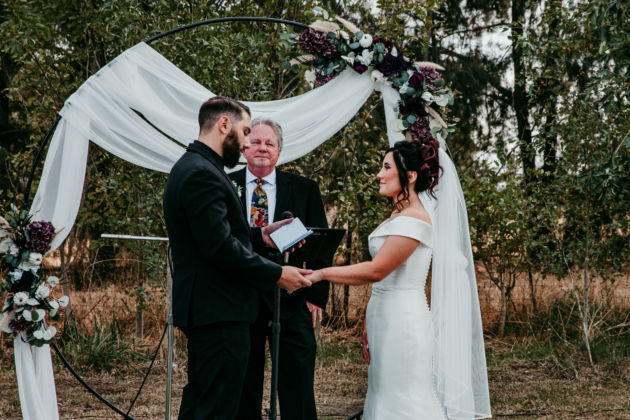Groom reading vows to his bride during their fall backyard ceremony under a floral arch in Vacaville, CA