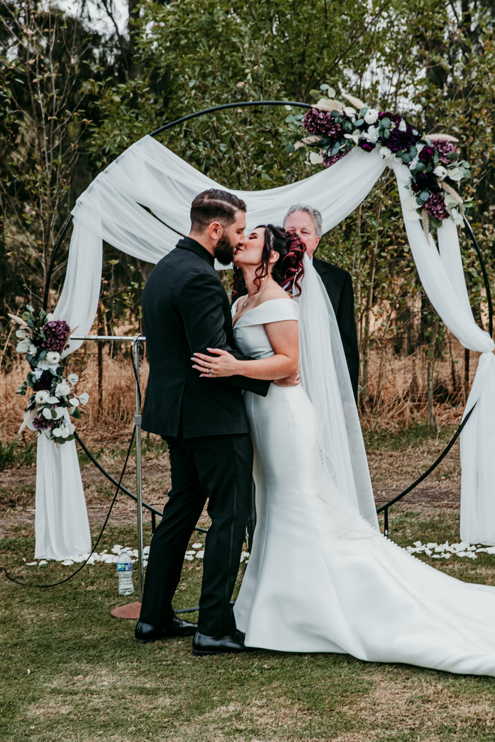 Bride and groom sharing their first kiss in front of a moody floral arch during an intimate outdoor wedding ceremony in Vacaville, CA