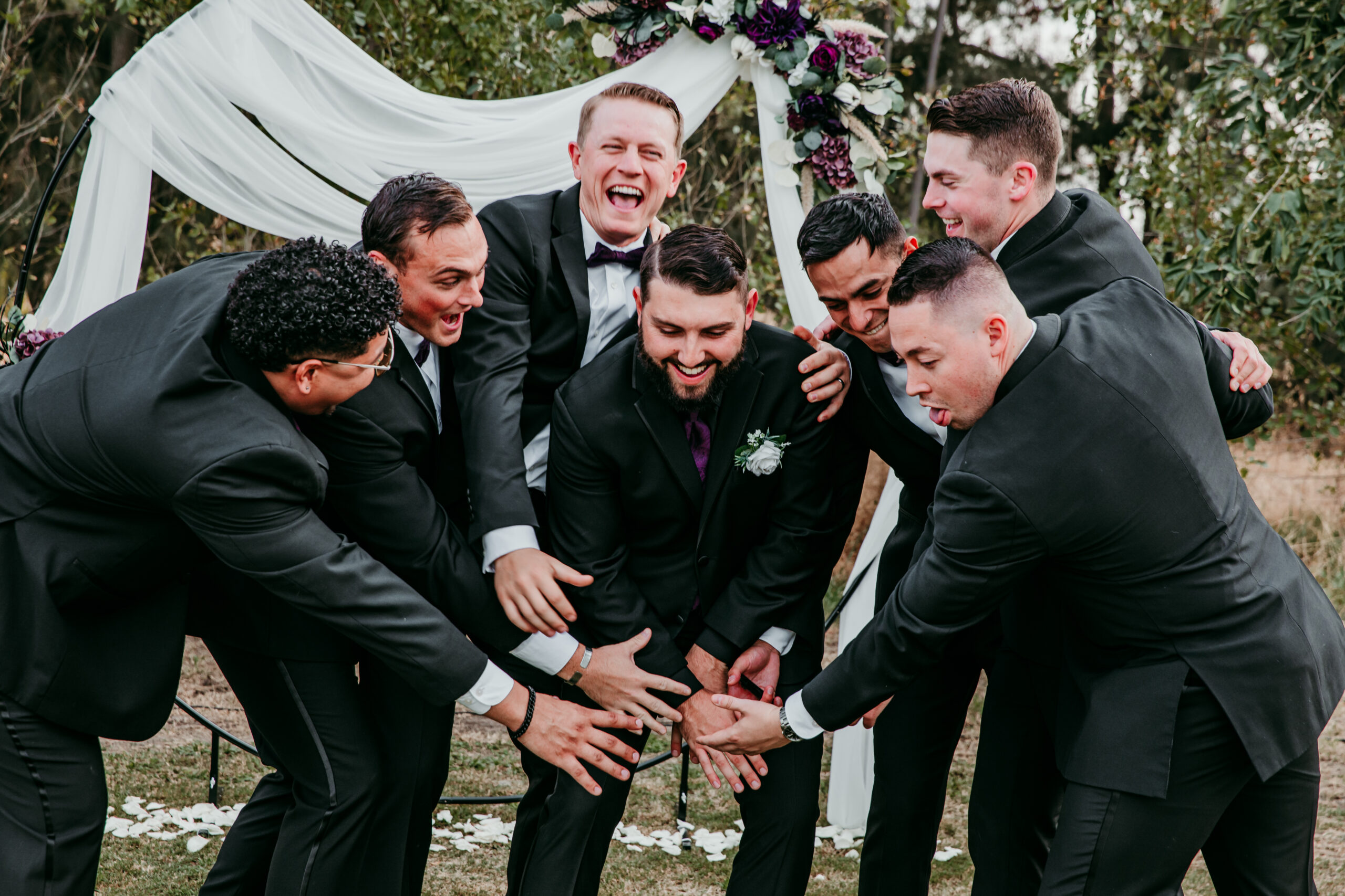 Groom and groomsmen huddling with big smiles and energy under the ceremony arch during a backyard wedding in Vacaville