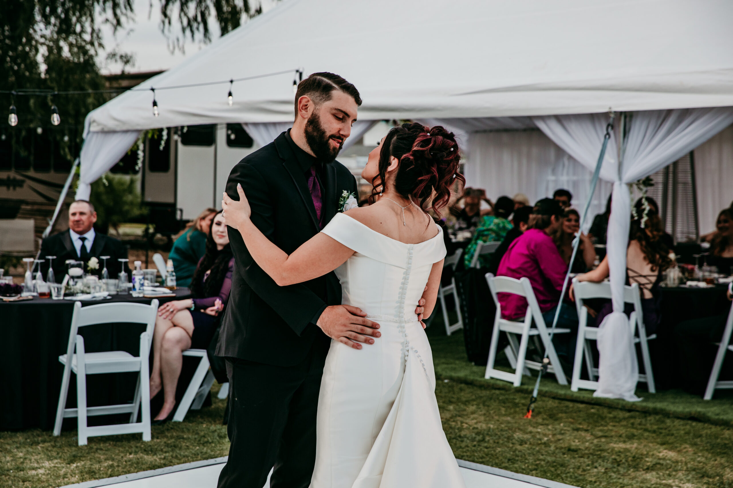 Couple dancing closely during their fall wedding reception with guests watching from white chairs under a tented space
