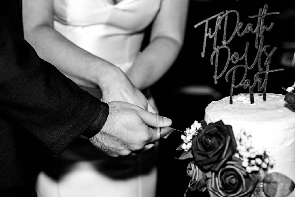 Close-up of the couple’s hands cutting a fall wedding cake with a gothic “Til Death Do Us Part” topper, documented by Bay Area wedding photographer.