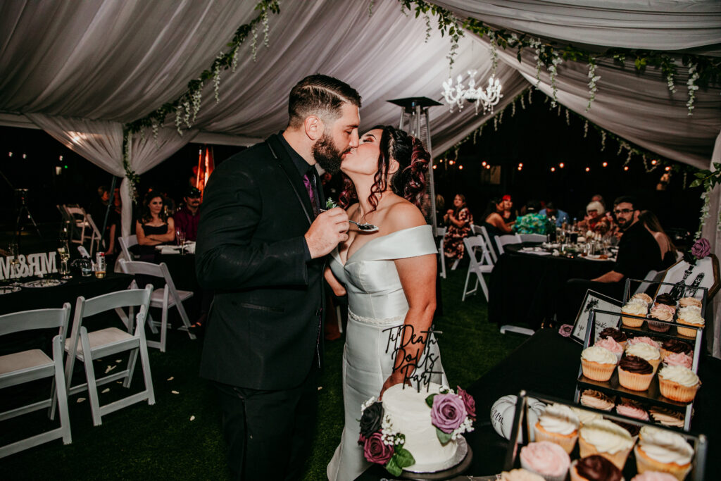 Bride and groom kissing after cake cutting at their Halloween-themed wedding reception, photographed by Bay Area wedding photographer.