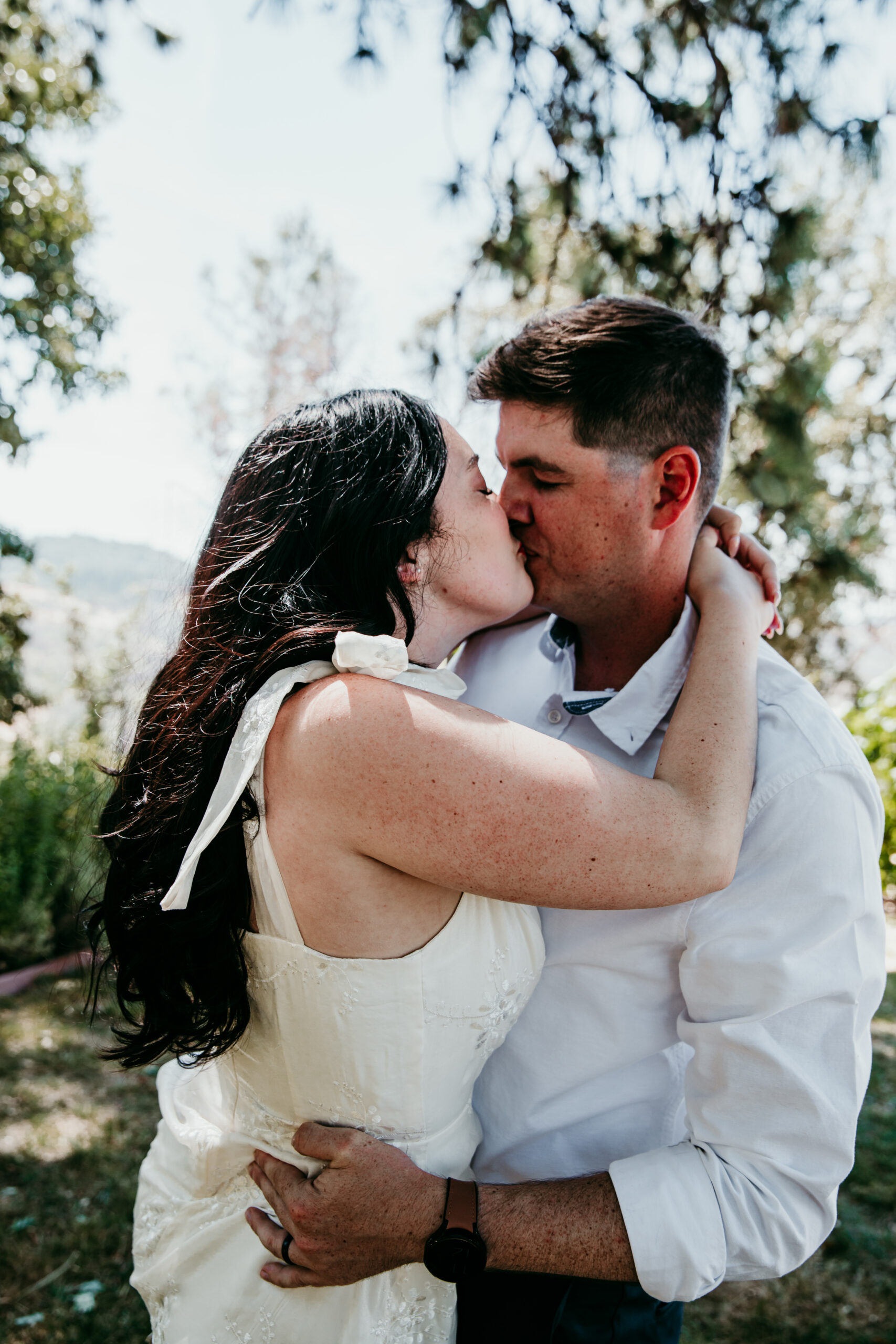 Bride and groom share a kiss during their Northern California elopement surrounded by trees and golden light.