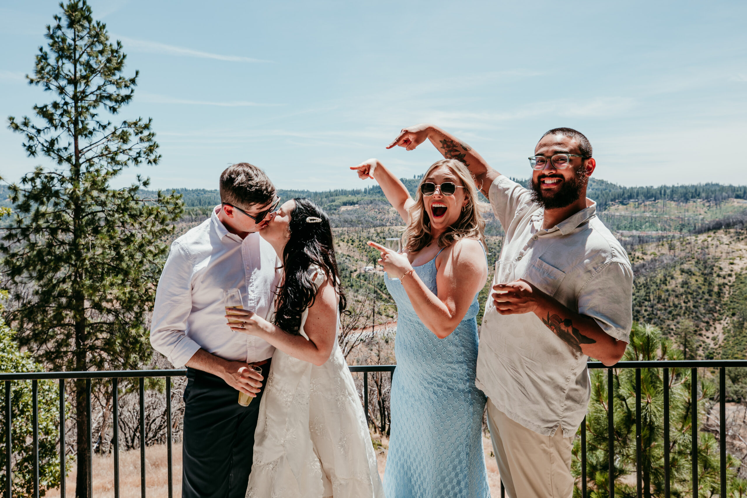 Bride and groom kiss while their two best friends cheer them on during a Northern California elopement celebration with stunning mountain views.