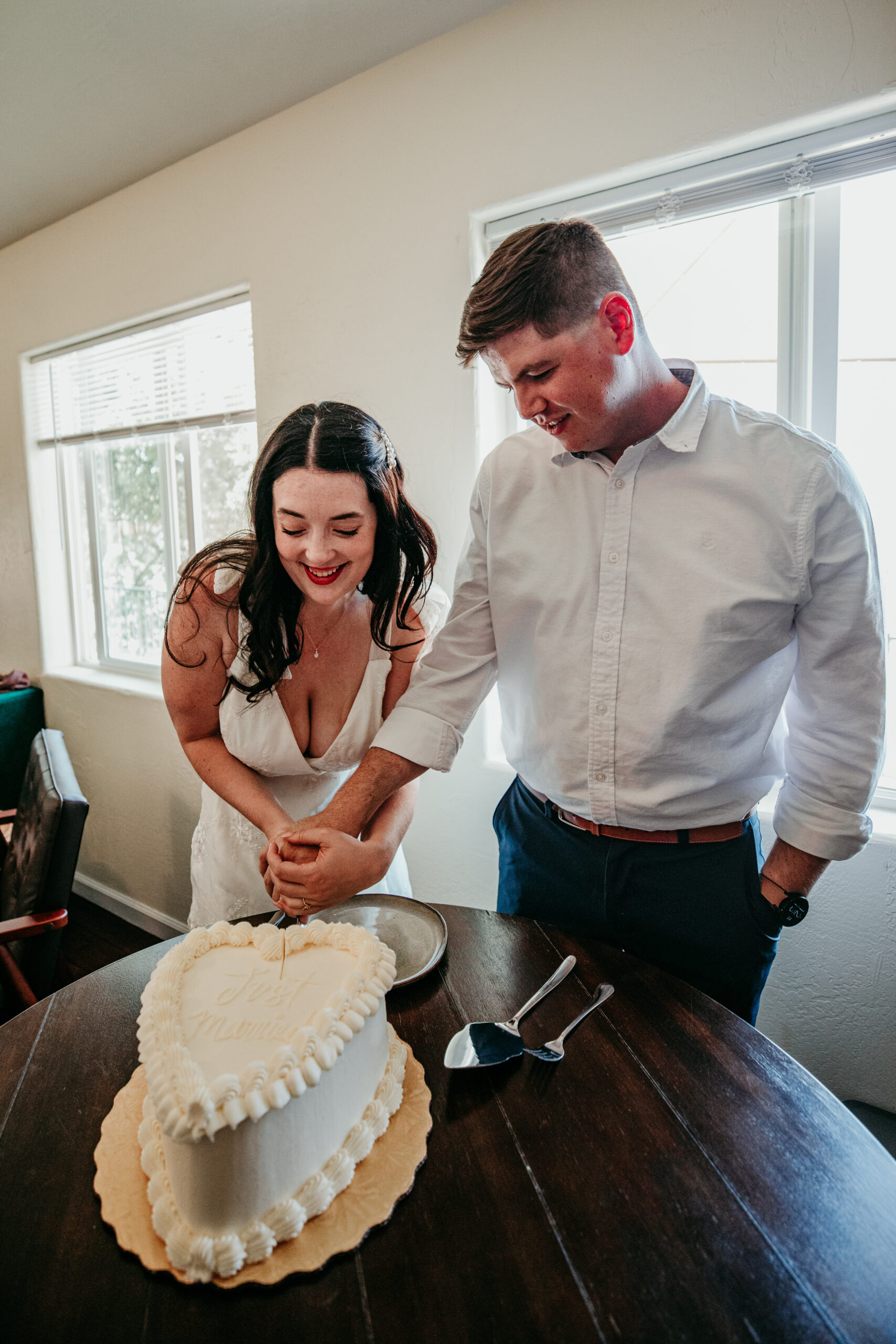 Bride and groom laugh while cutting their heart-shaped wedding cake during their Northern California elopement celebration.