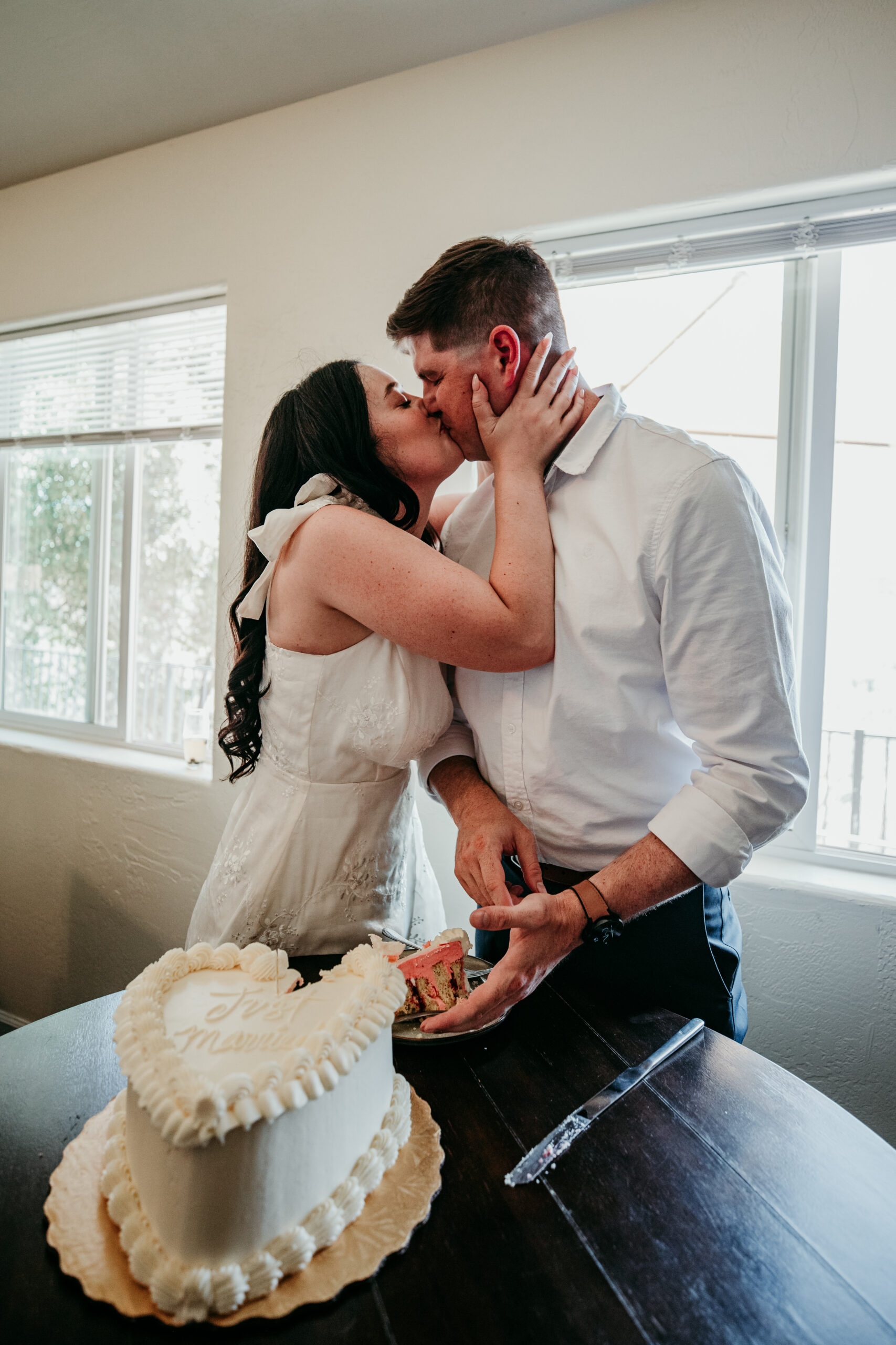 Bride kisses her groom while holding a slice of cake during their joyful Northern California elopement celebration.