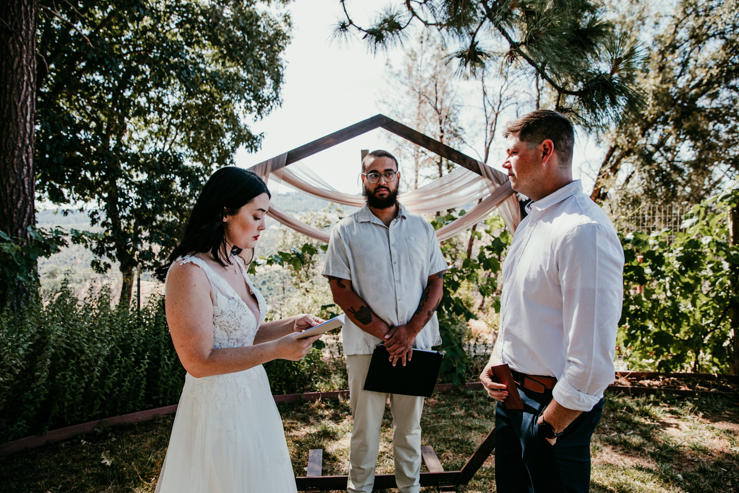 Bride reading her vows during an intimate elopement ceremony at a Grass Valley CA Airbnb, with the officiant and groom looking on.