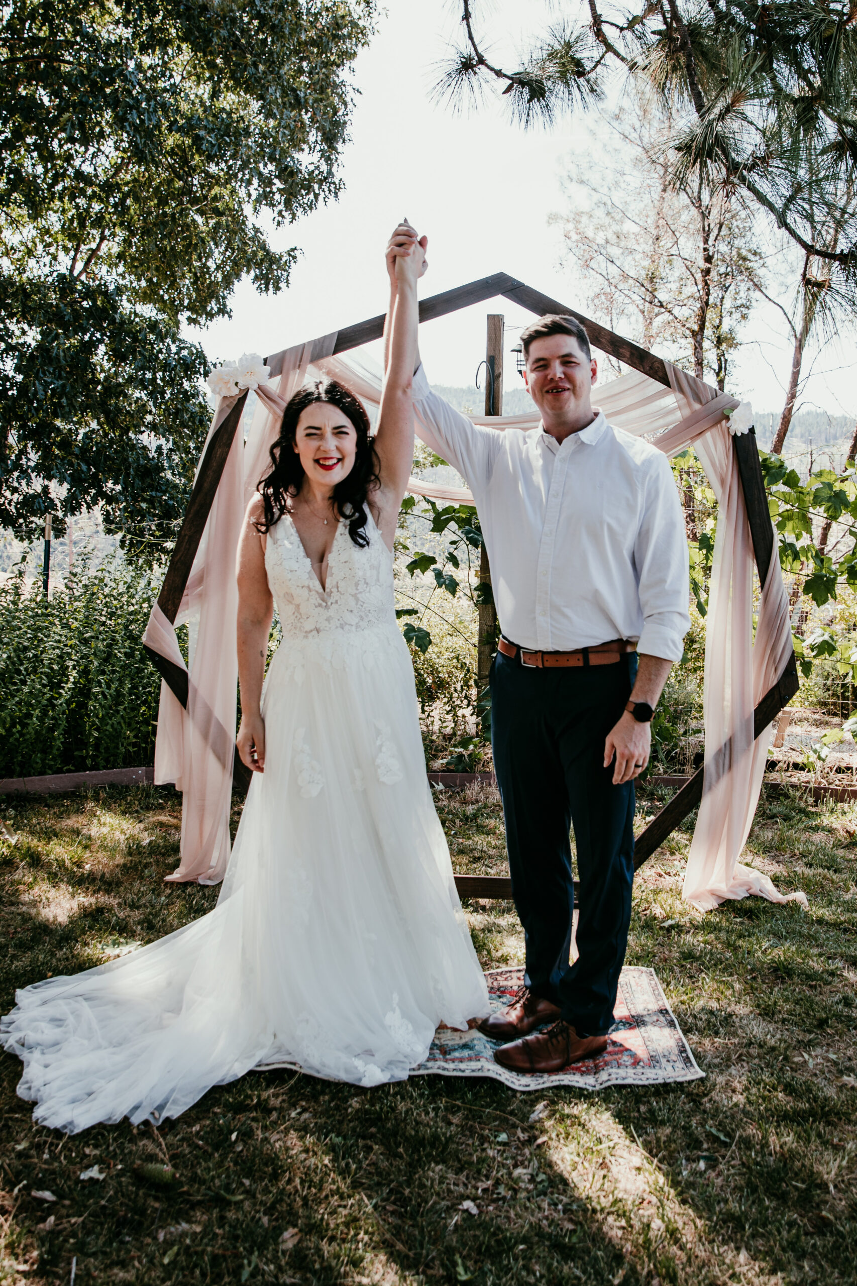 Just married! Bride and groom raise their hands in celebration at their relaxed backyard elopement in Grass Valley CA.