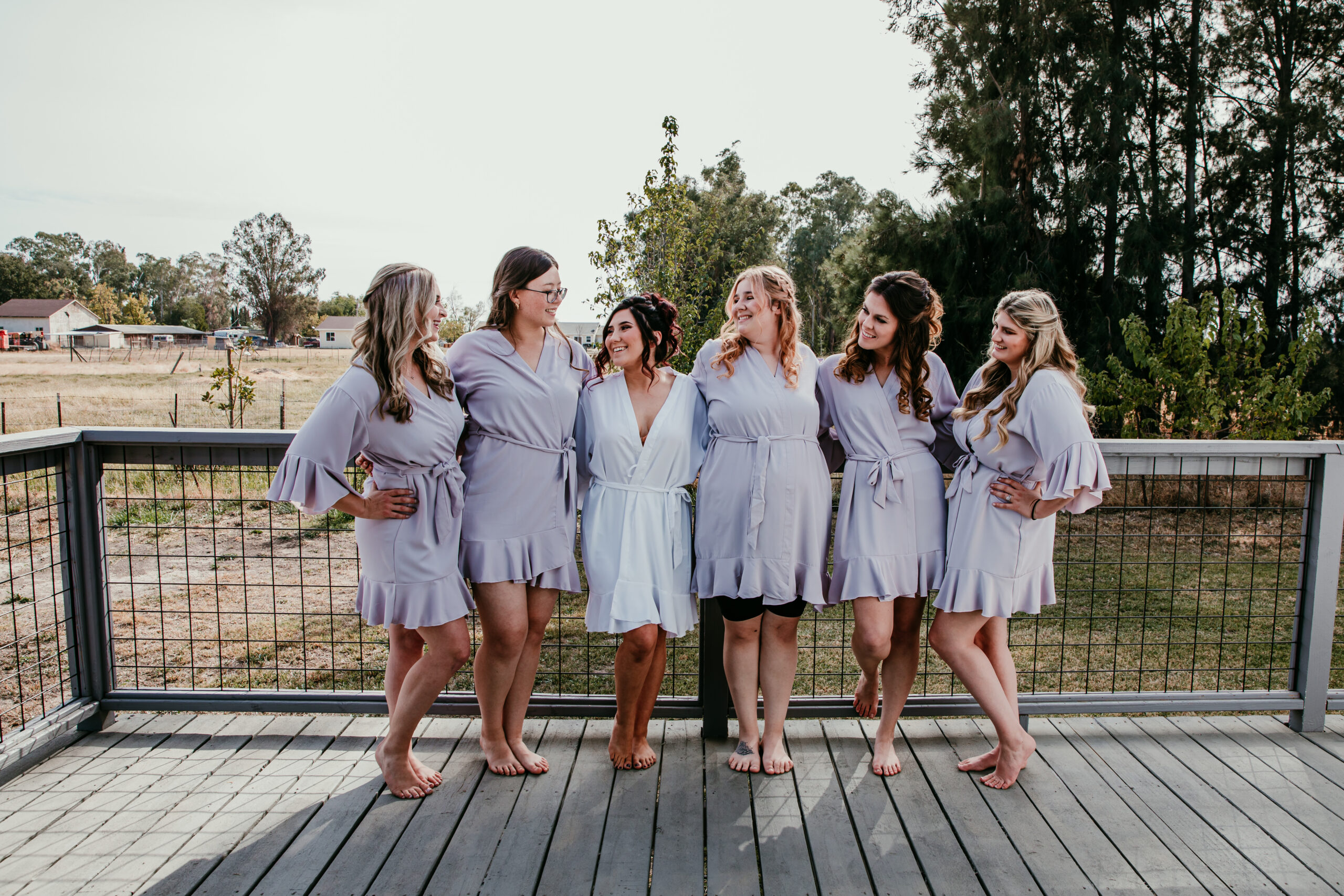 Bride and bridesmaids wearing matching robes sharing a fun moment on the deck before the backyard wedding in Vacaville, CA