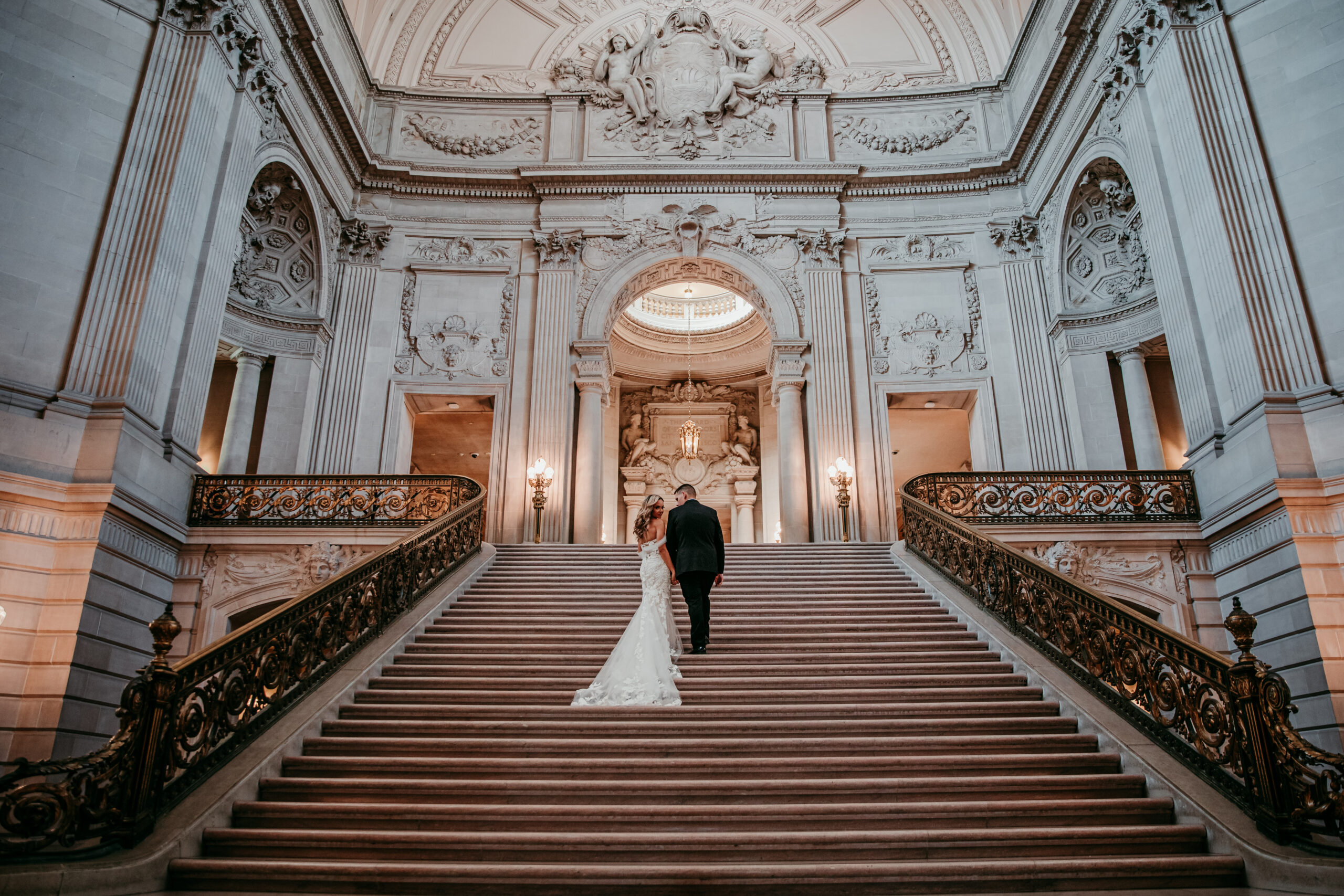Bride and groom walking up the grand staircase inside San Francisco City Hall, one of the most elegant places for getting married in California.