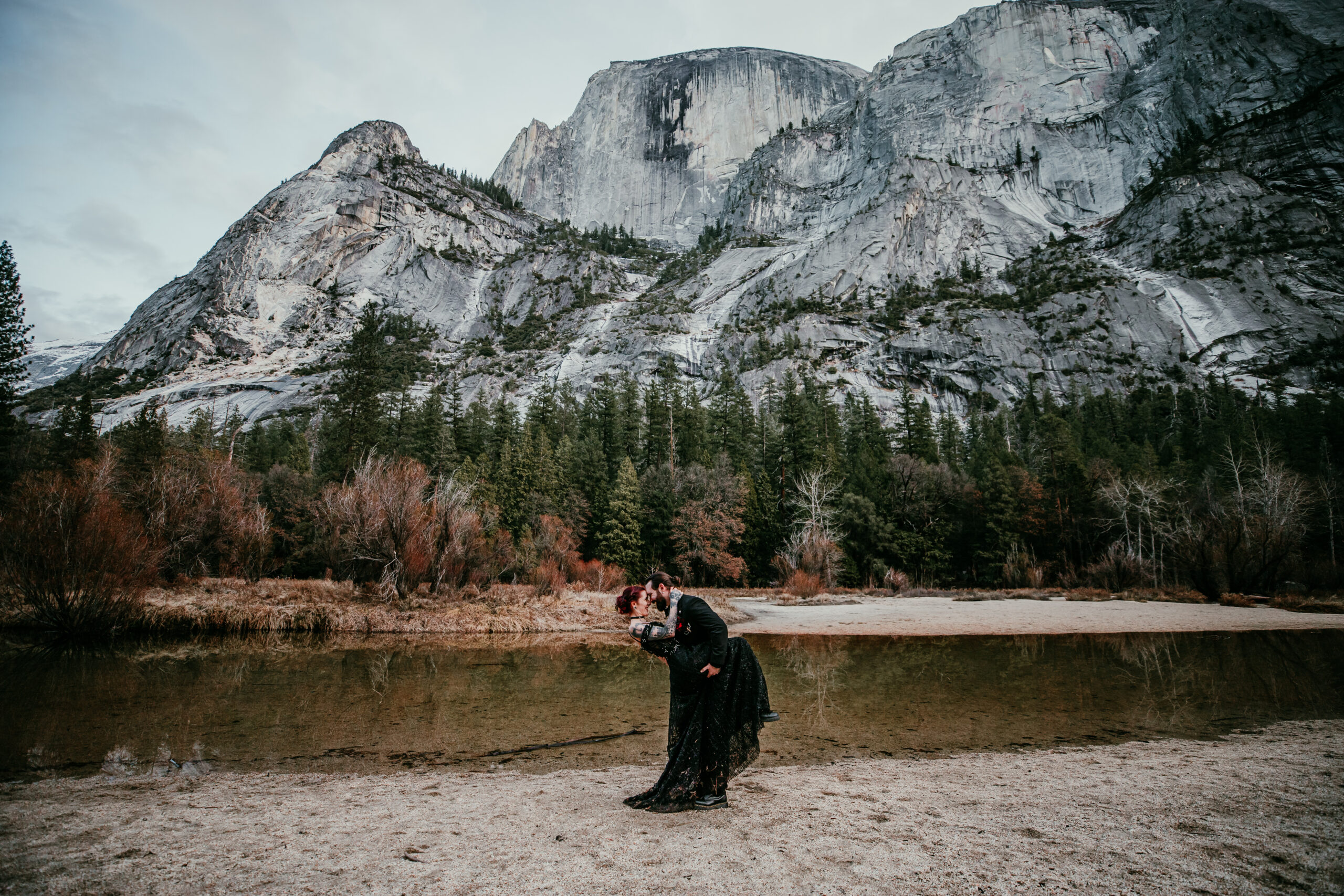 Romantic Yosemite elopement inspiration featuring a couple sharing a kiss in front of dramatic granite cliffs and Mirror Lake in winter