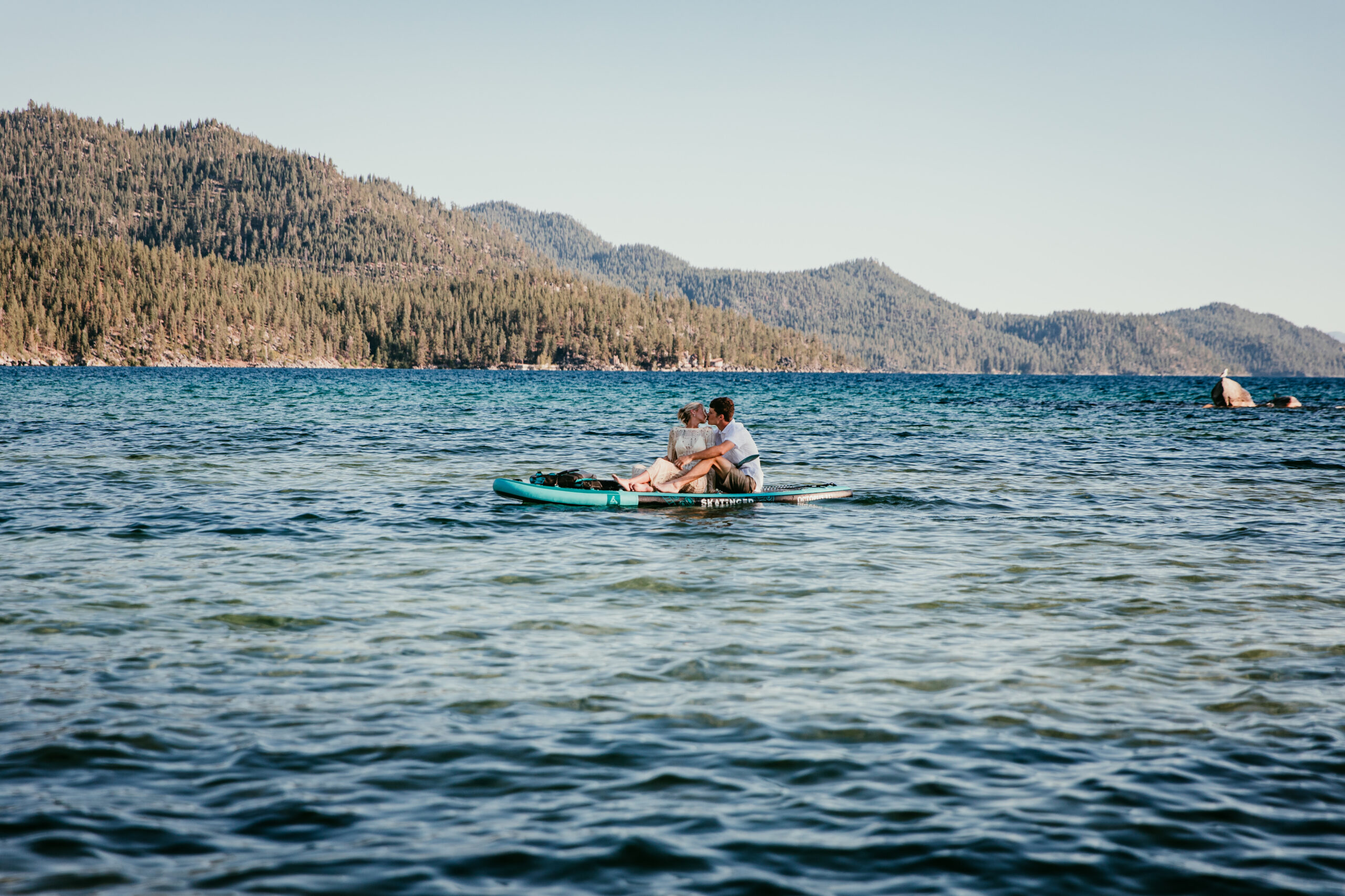 Couple kissing while sitting together on a paddleboard during their Lake Tahoe elopement, surrounded by blue water and forested mountains.