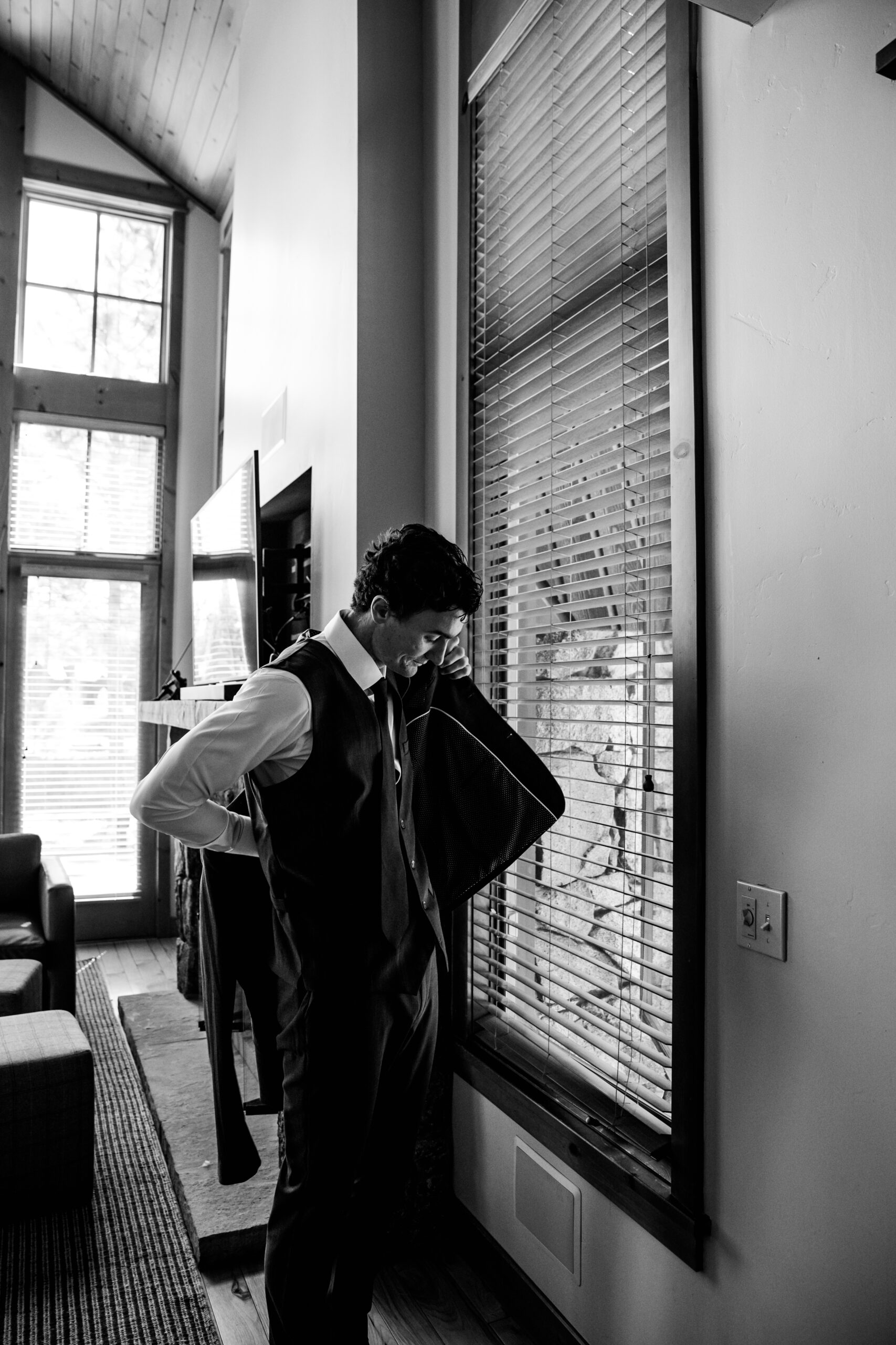 Groom adjusting his suit jacket by the window while getting ready for a Lake Tahoe elopement, captured in timeless black and white lake tahoe elopement photos.