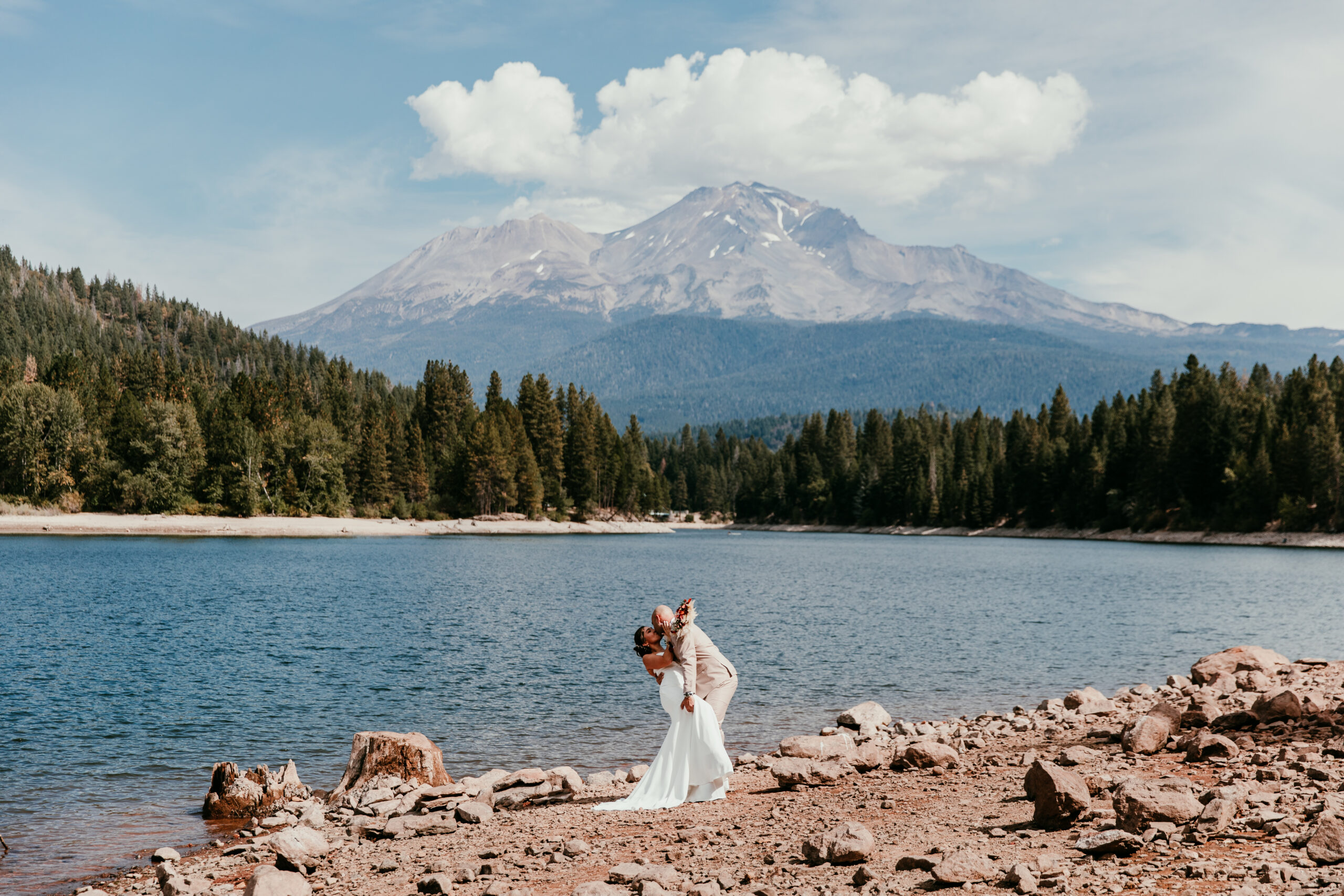 Newlyweds kissing beside a mountain lake with Mount Shasta in the background during their Northern California elopement.
