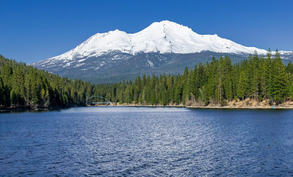 Snow-covered Mount Shasta rising above Lake Siskiyou and the surrounding evergreen forest during winter.
