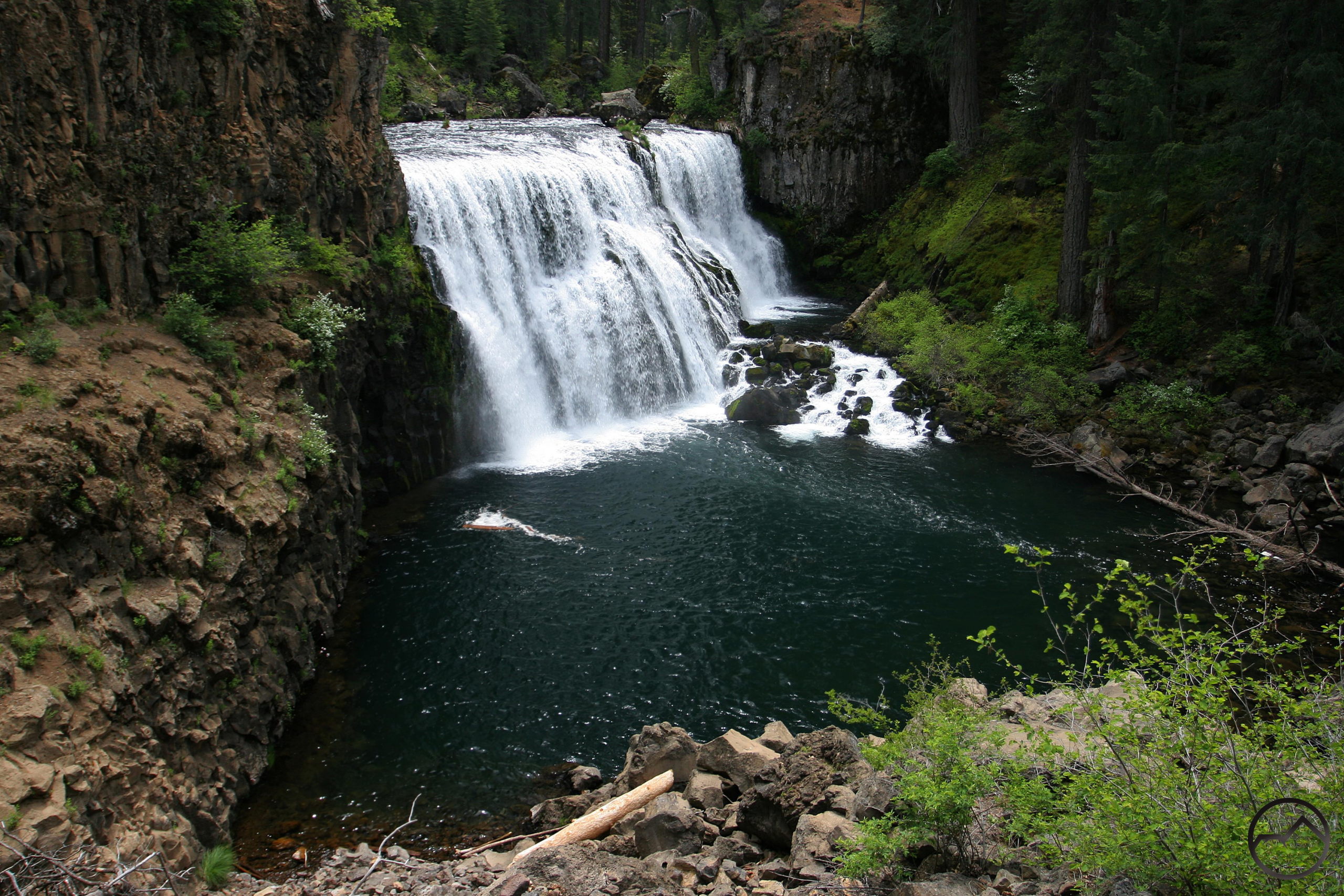 Middle McCloud Falls cascading into a deep emerald pool, surrounded by moss-covered cliffs and evergreen forest near Mount Shasta, California.