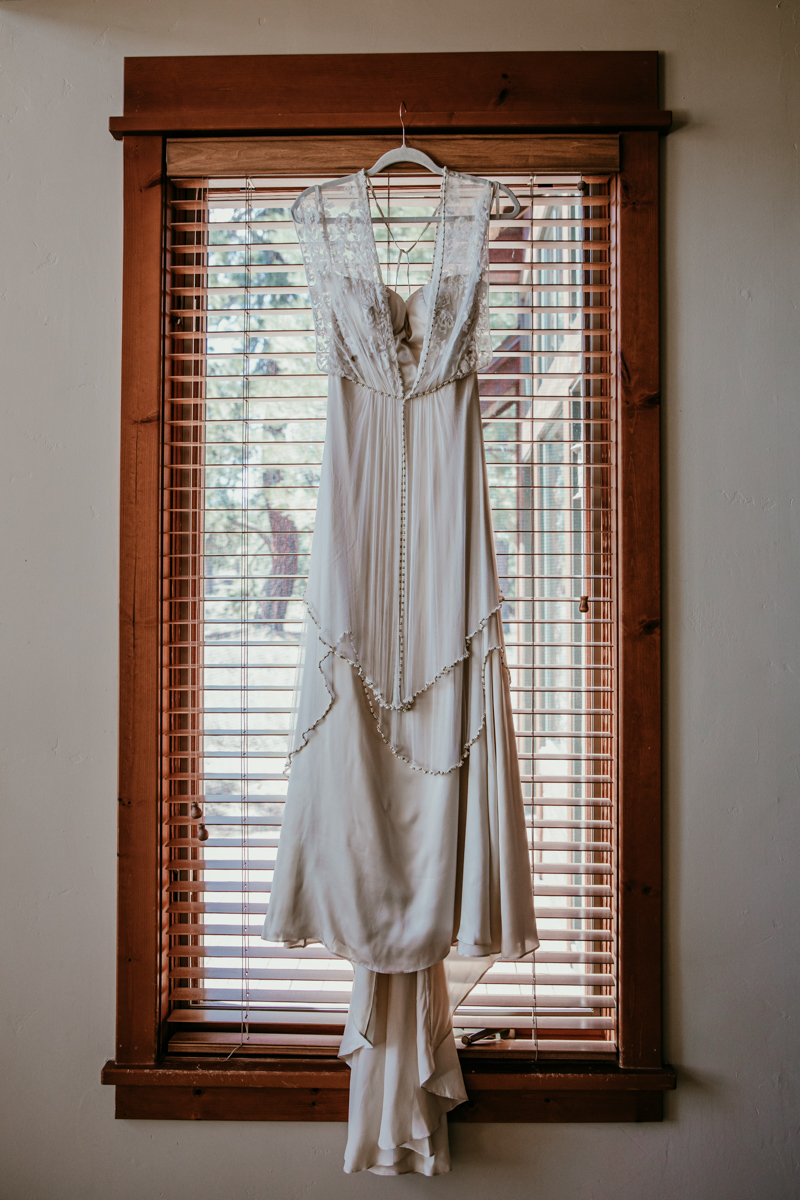 Lace and satin wedding dress hanging in a sunlit window before the elopement