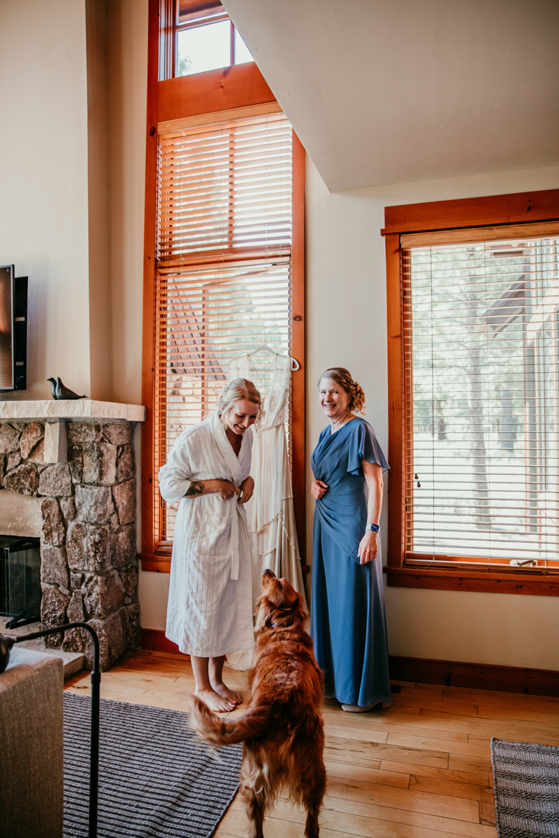 Bride laughing with a bridesmaid while her golden retriever looks up at her during the getting ready moments