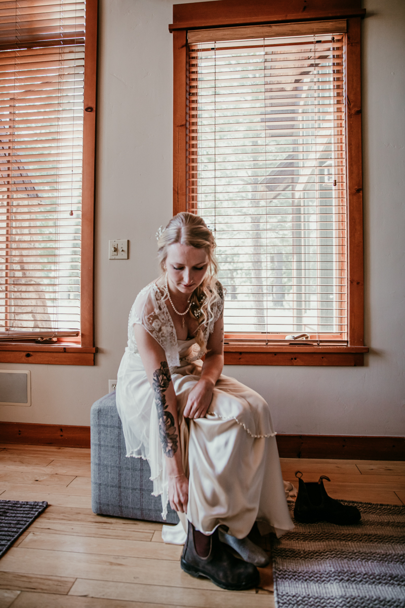 Bride sitting by the window and putting on her Blundstone boots before her elopement