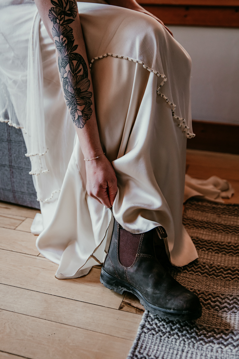 Bride slipping on a pair of Blundstone boots under her wedding dress before the elopement