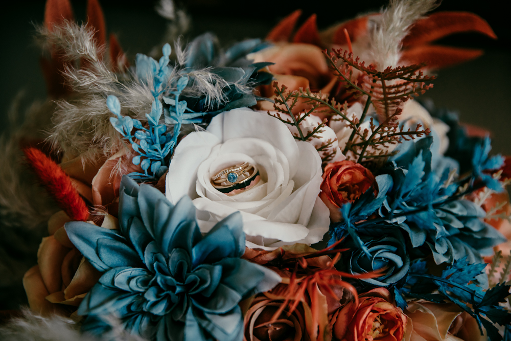 Wedding rings placed inside a white rose surrounded by vibrant blue and rust florals