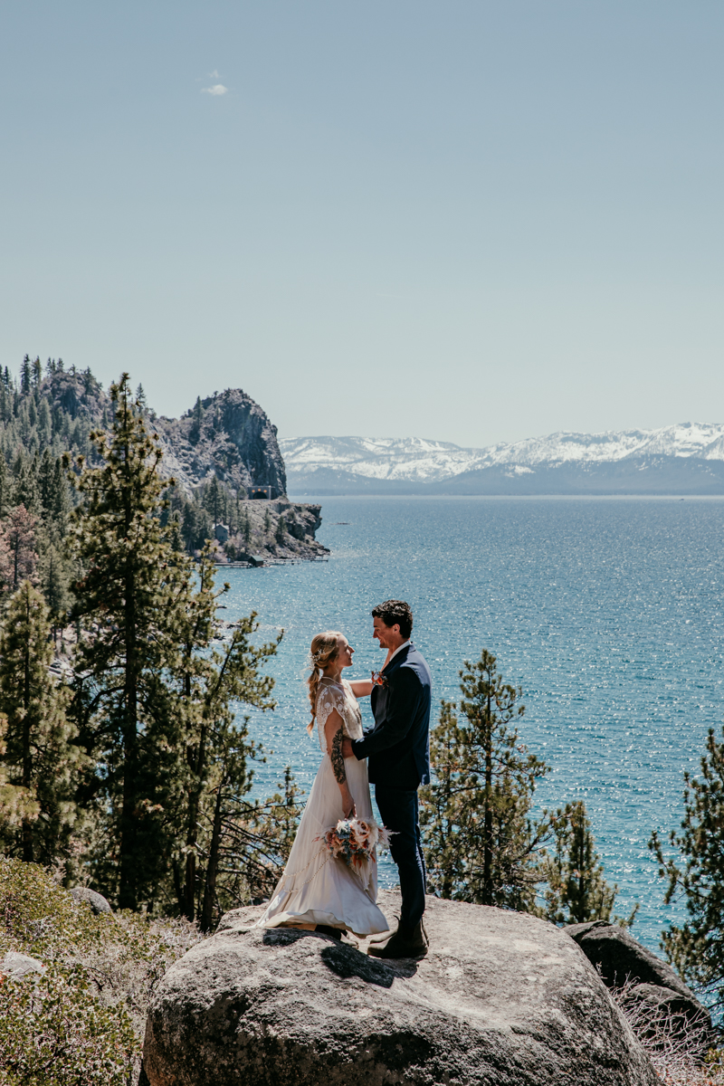 Bride and groom standing on a rock with panoramic views of Lake Tahoe during their Logan Shoals elopement