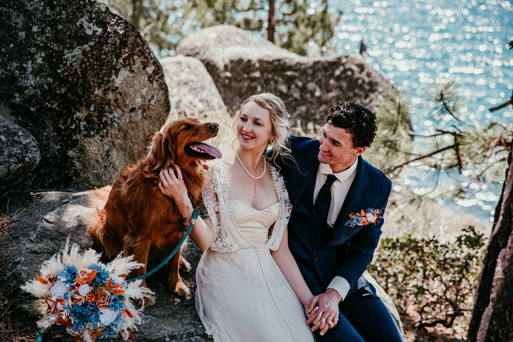Bride and groom sitting on a rock at Logan Shoals Vista Point with their golden retriever, bouquet nearby, overlooking Lake Tahoe