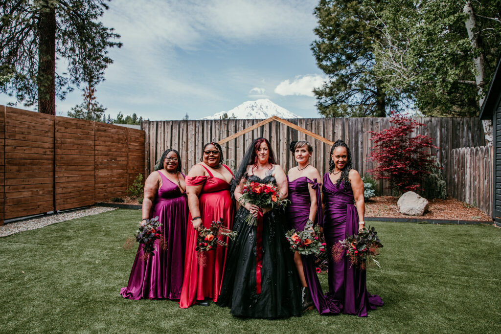 Bride in a black wedding dress standing with her bridesmaids in colorful gowns at Shasta View Lodge while eloping in Mount Shasta.