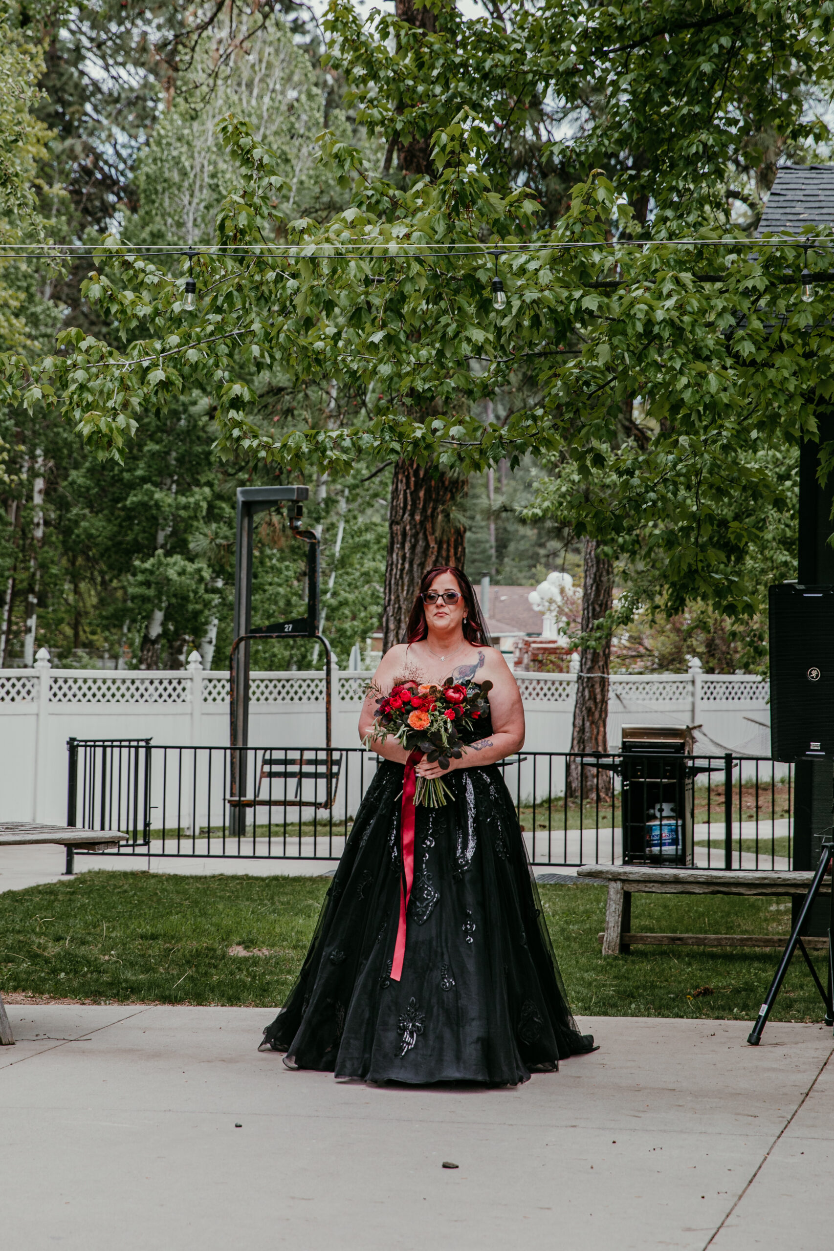 Bride wearing a black wedding dress and holding a red bouquet as she walks toward the ceremony while eloping in Mount Shasta.