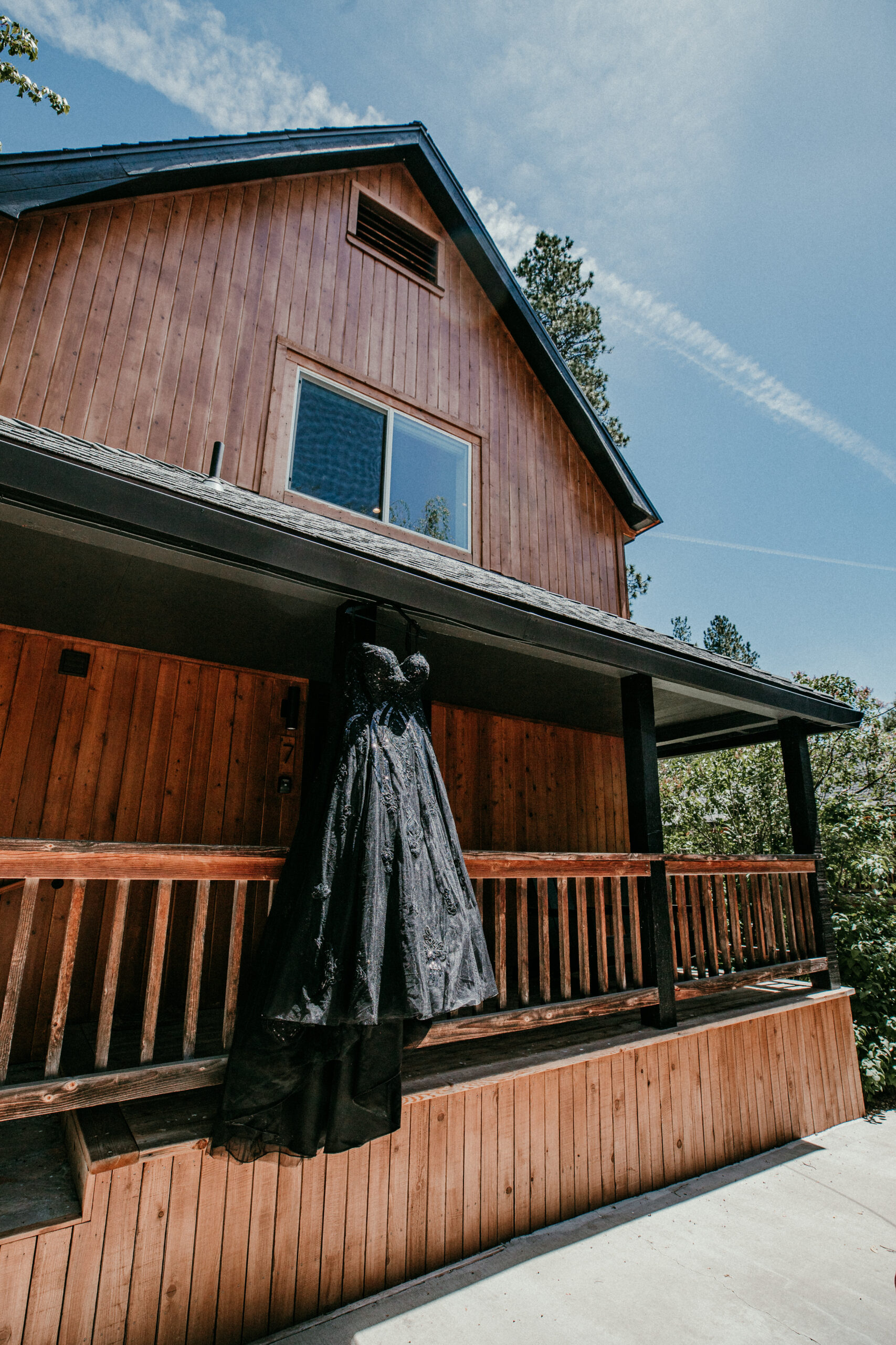 Black wedding dress hanging outside a wood cabin before eloping in Mount Shasta, showcasing unique elopement attire for a nontraditional bride.