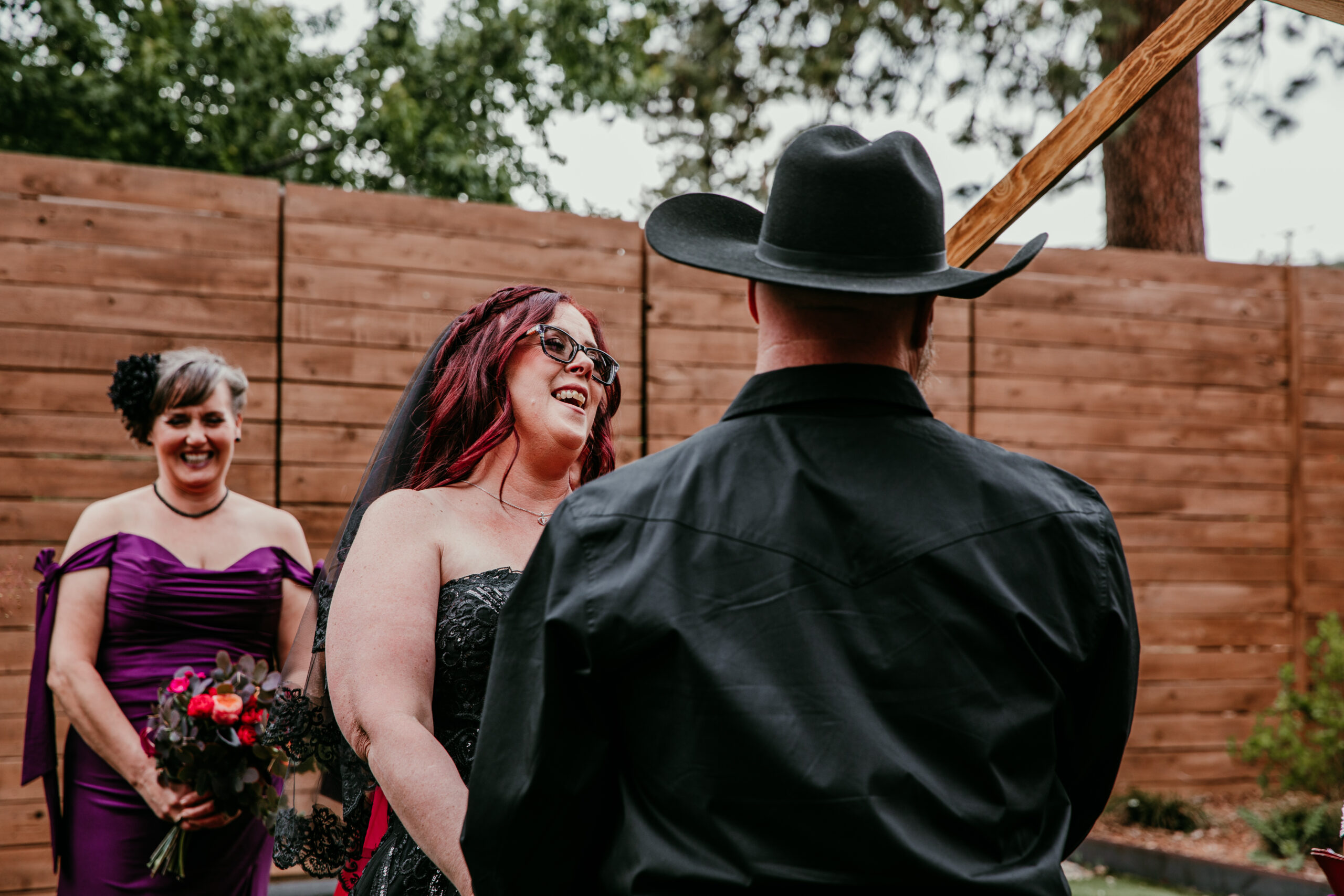 Bride smiling at the groom during their ceremony while eloping in Mount Shasta, with a bridesmaid standing nearby holding a bouquet.