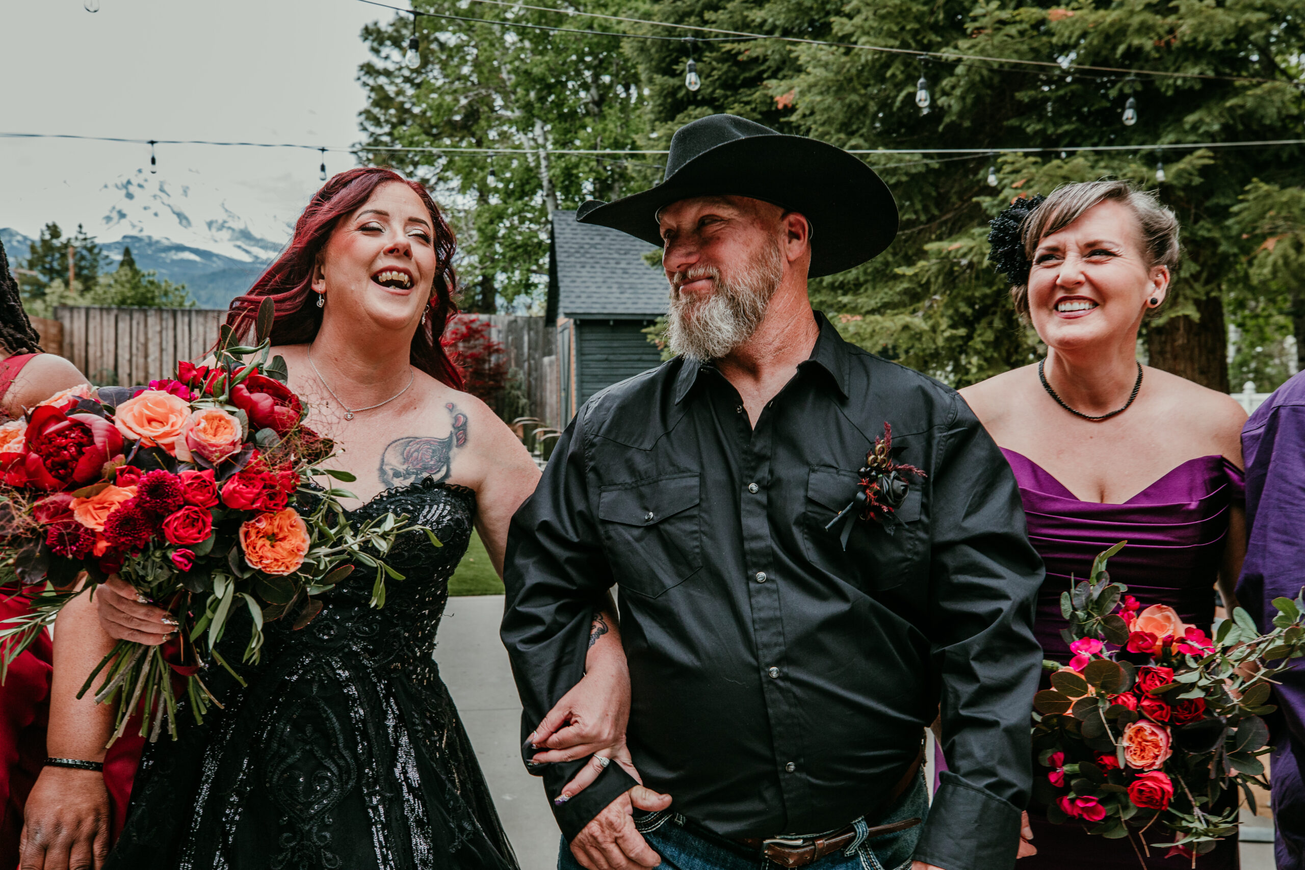 Bride laughing with the groom and bridesmaid while eloping in Mount Shasta, holding a bold bouquet of red and orange flowers.