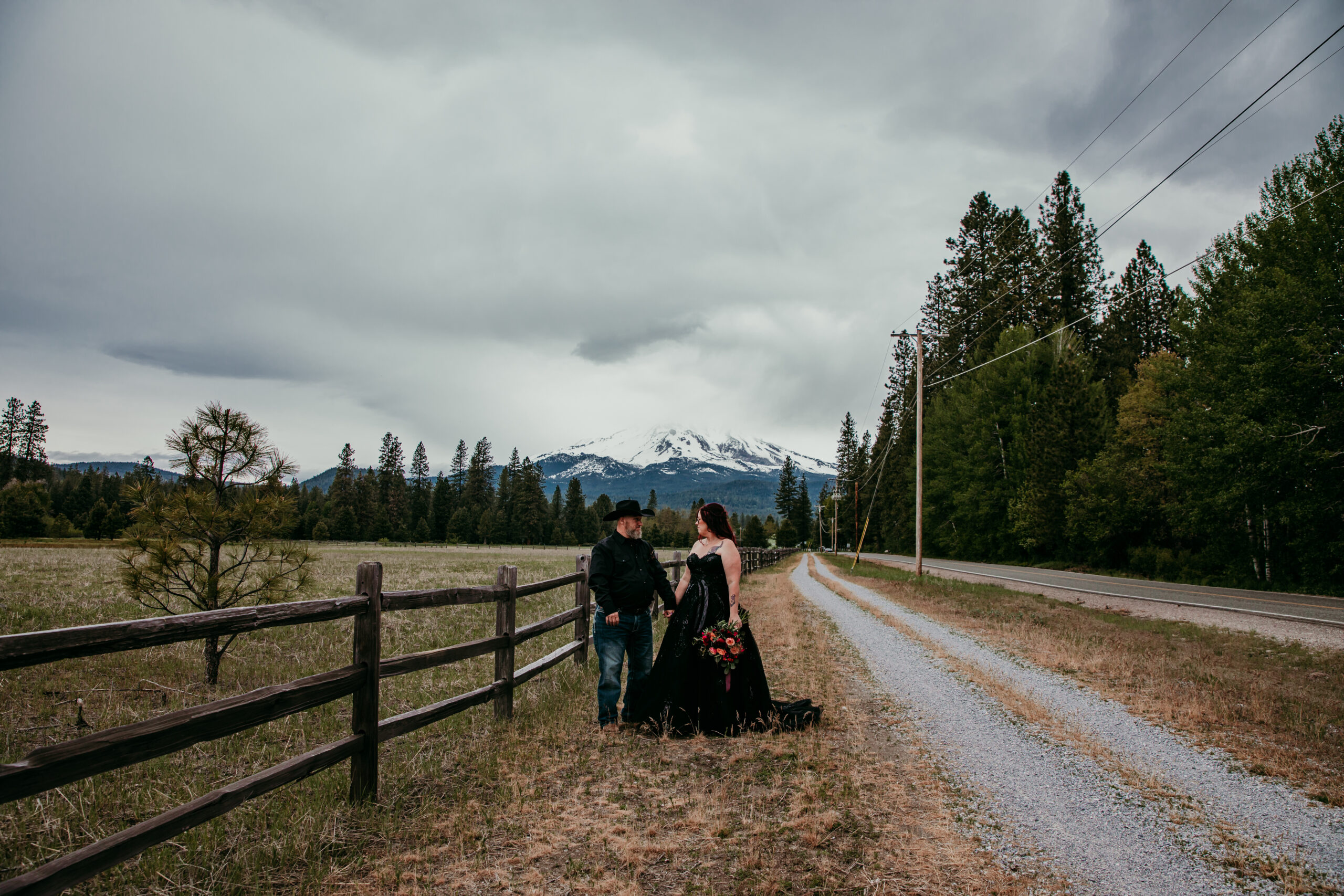 Couple standing on a country road with Mount Shasta in the distance, one of the most romantic places to elope in California, surrounded by pine trees and open fields.