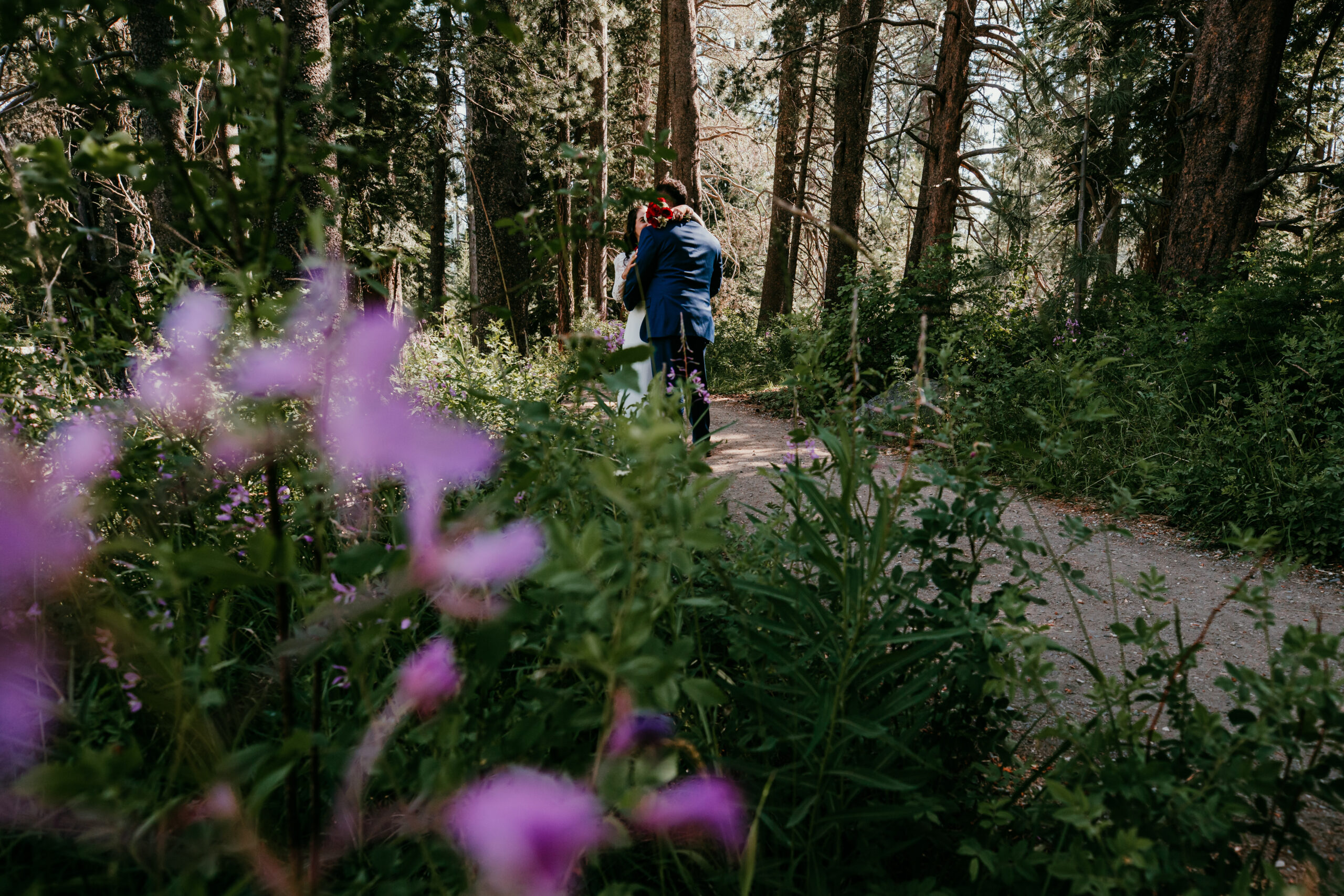 Bride and groom walking together through a forest trail with wildflowers during their elopement in Lake Tahoe.