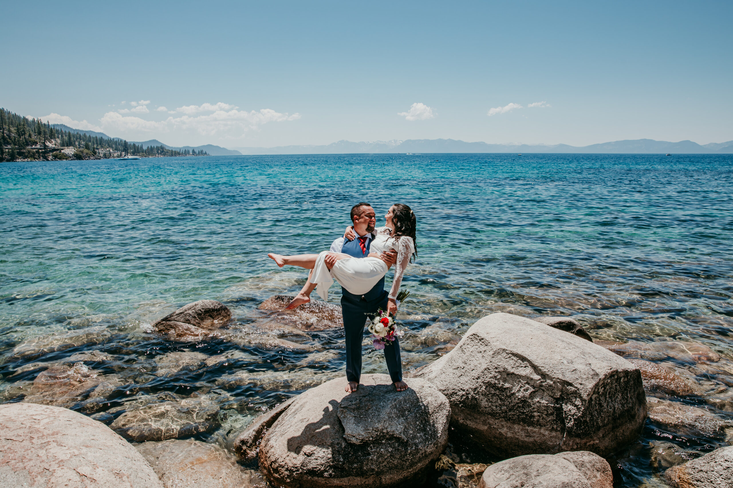 Groom holding bride on rocks by the turquoise water during their elopement in Lake Tahoe.