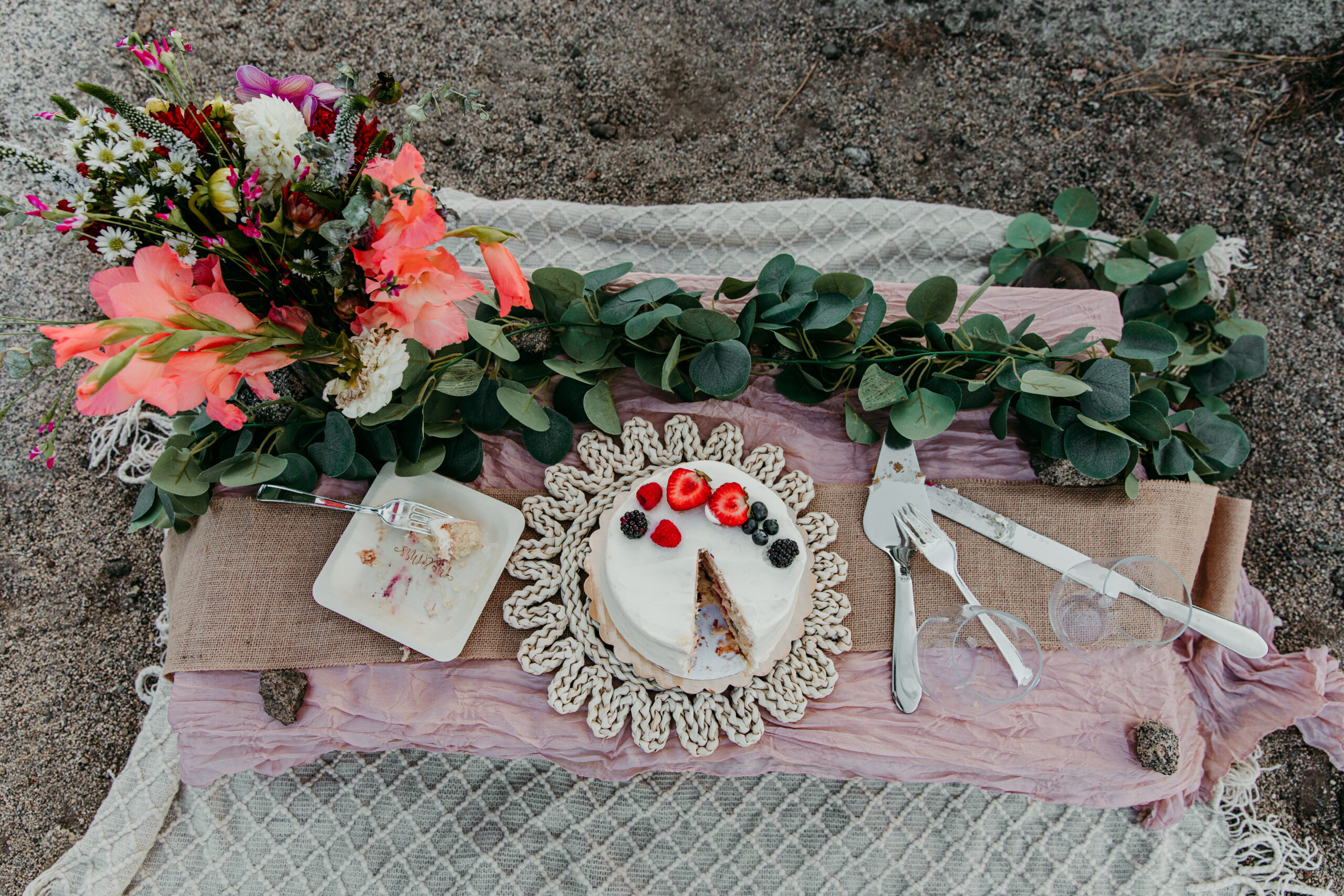 Elopement in Lake Tahoe picnic table setup with a floral arrangement, eucalyptus greenery, and a berry-topped wedding cake on a rustic blanket.