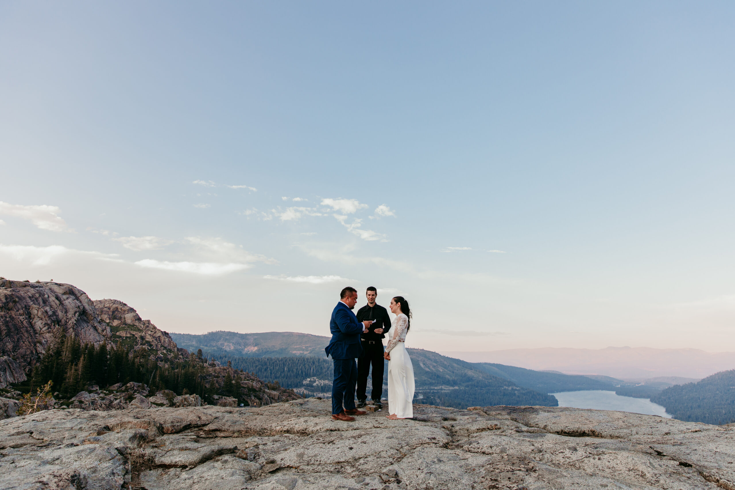 Elopement in Lake Tahoe with a couple standing on a rocky cliff during their ceremony, overlooking the lake and mountains at sunset.