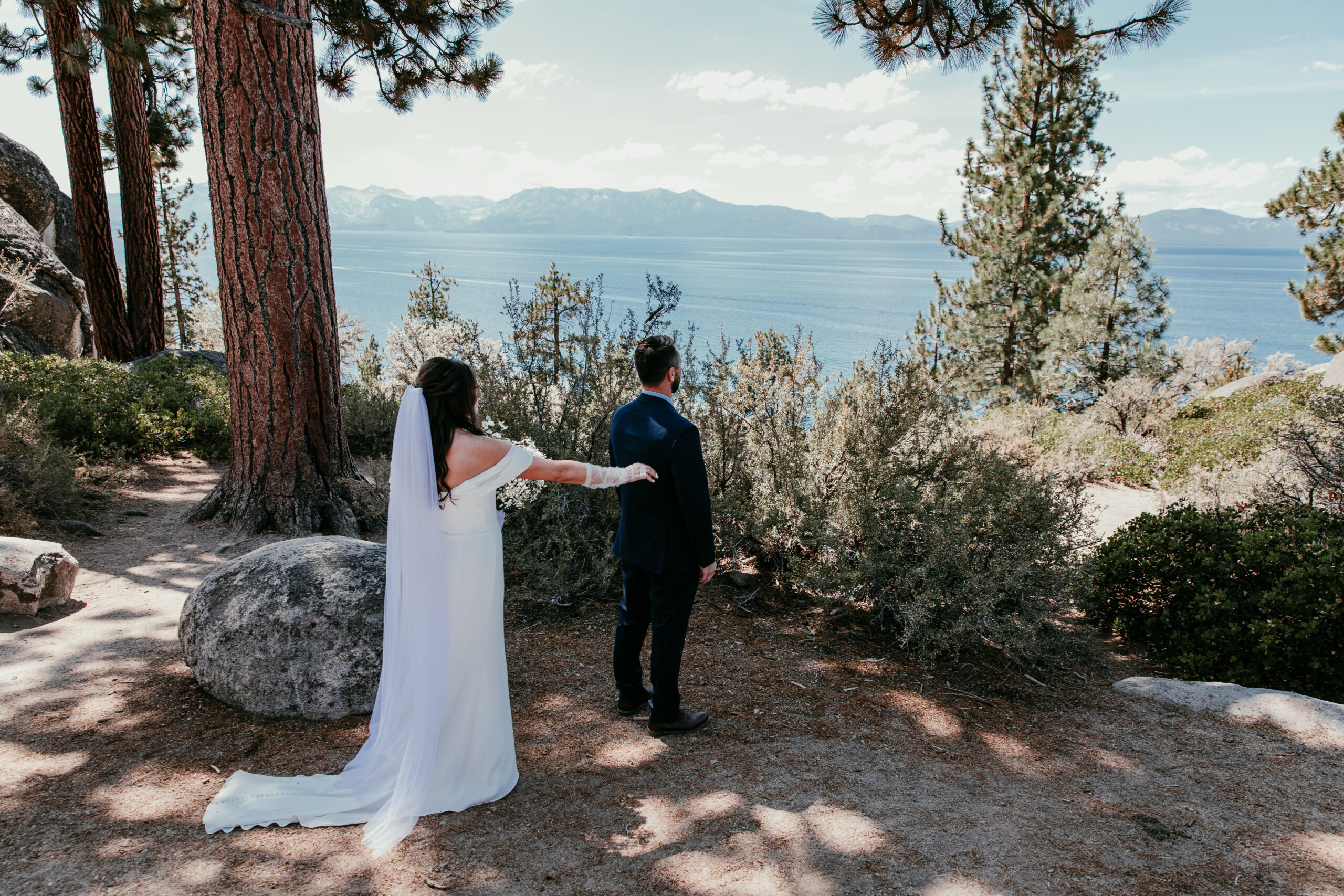 Bride reaching for groom during their first look overlooking the lake at their elopement Lake Tahoe.