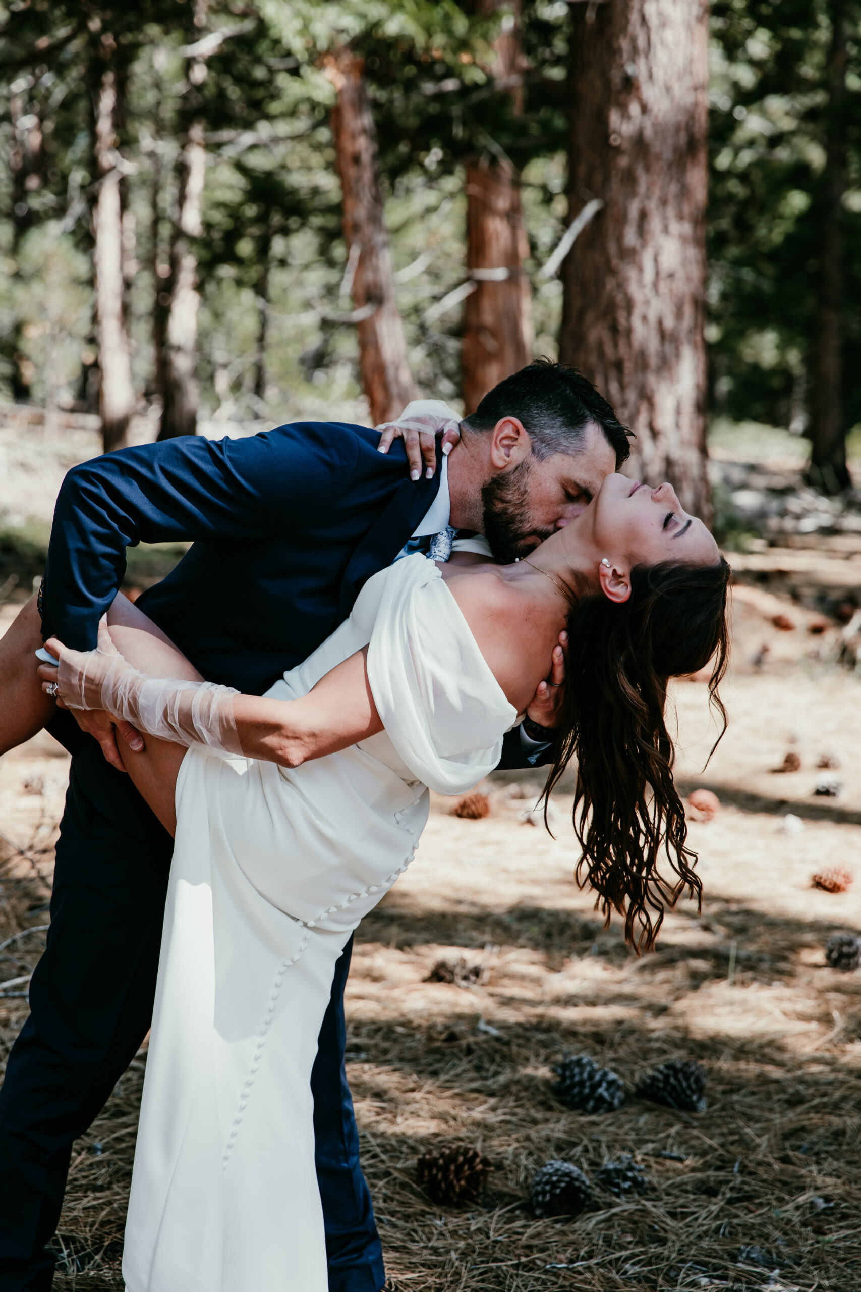 Groom dipping and kissing bride among pine trees during their elopement Lake Tahoe.
