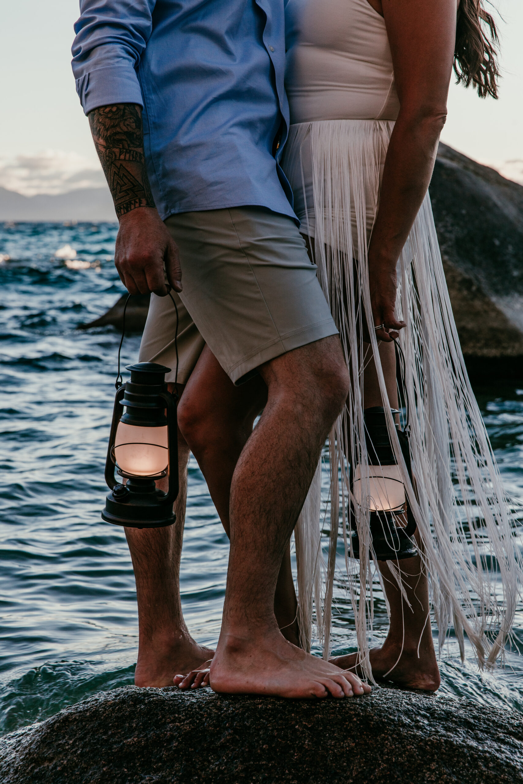Bride and groom holding lanterns while standing barefoot on rocks during their elopement Lake Tahoe.