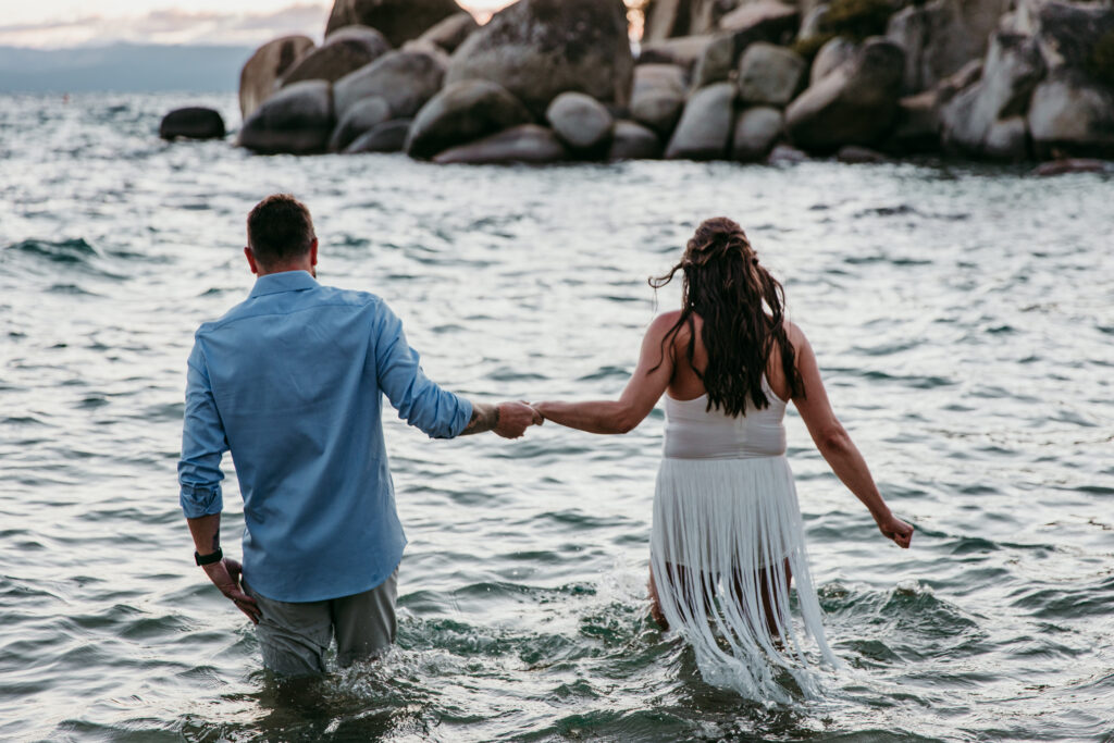Couple walking hand in hand into Lake Tahoe water highlighting playful elopement ideas in California