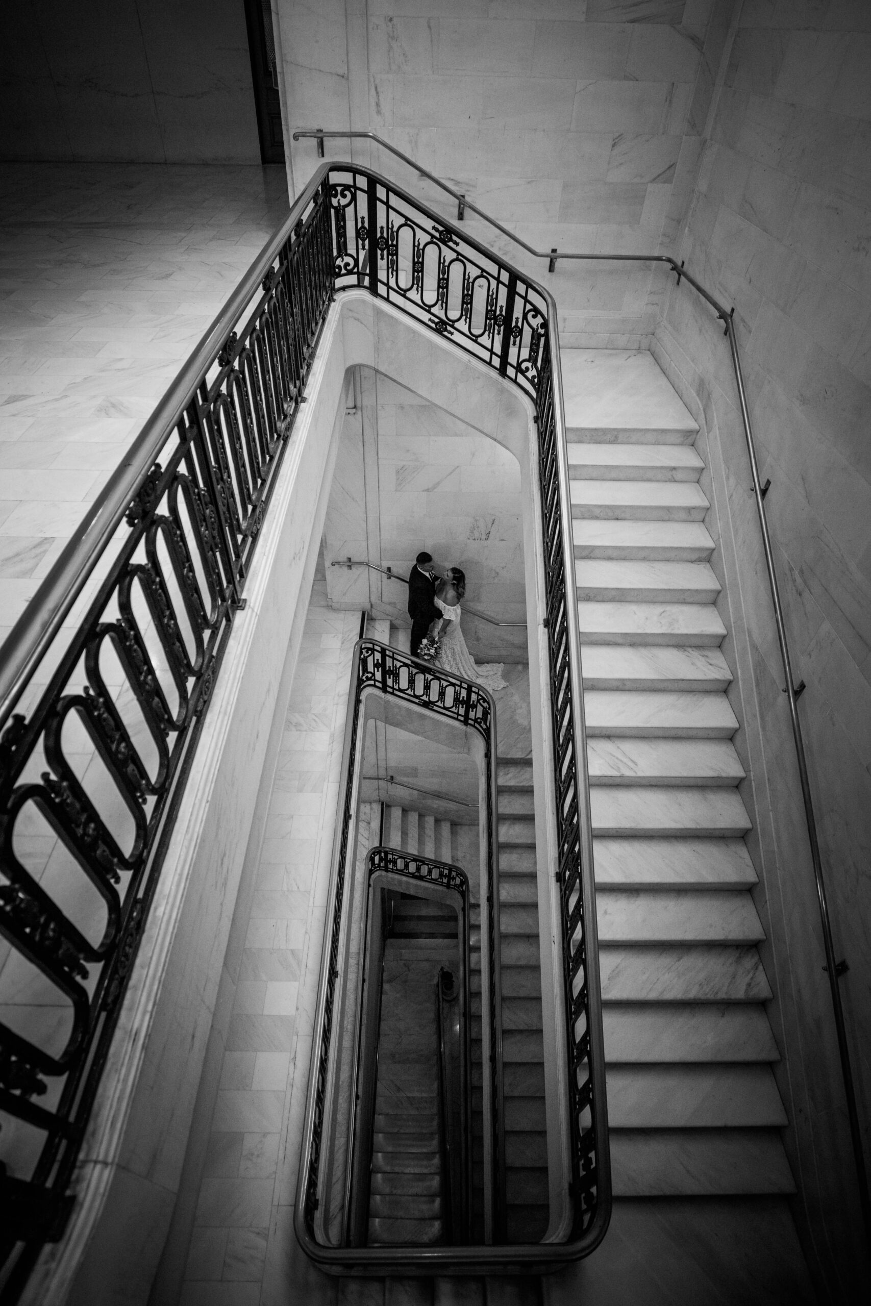 Black and white aerial photo of a couple embracing on the marble staircase inside San Francisco City Hall during their elopement, captured by a san francisco elopement photographer.