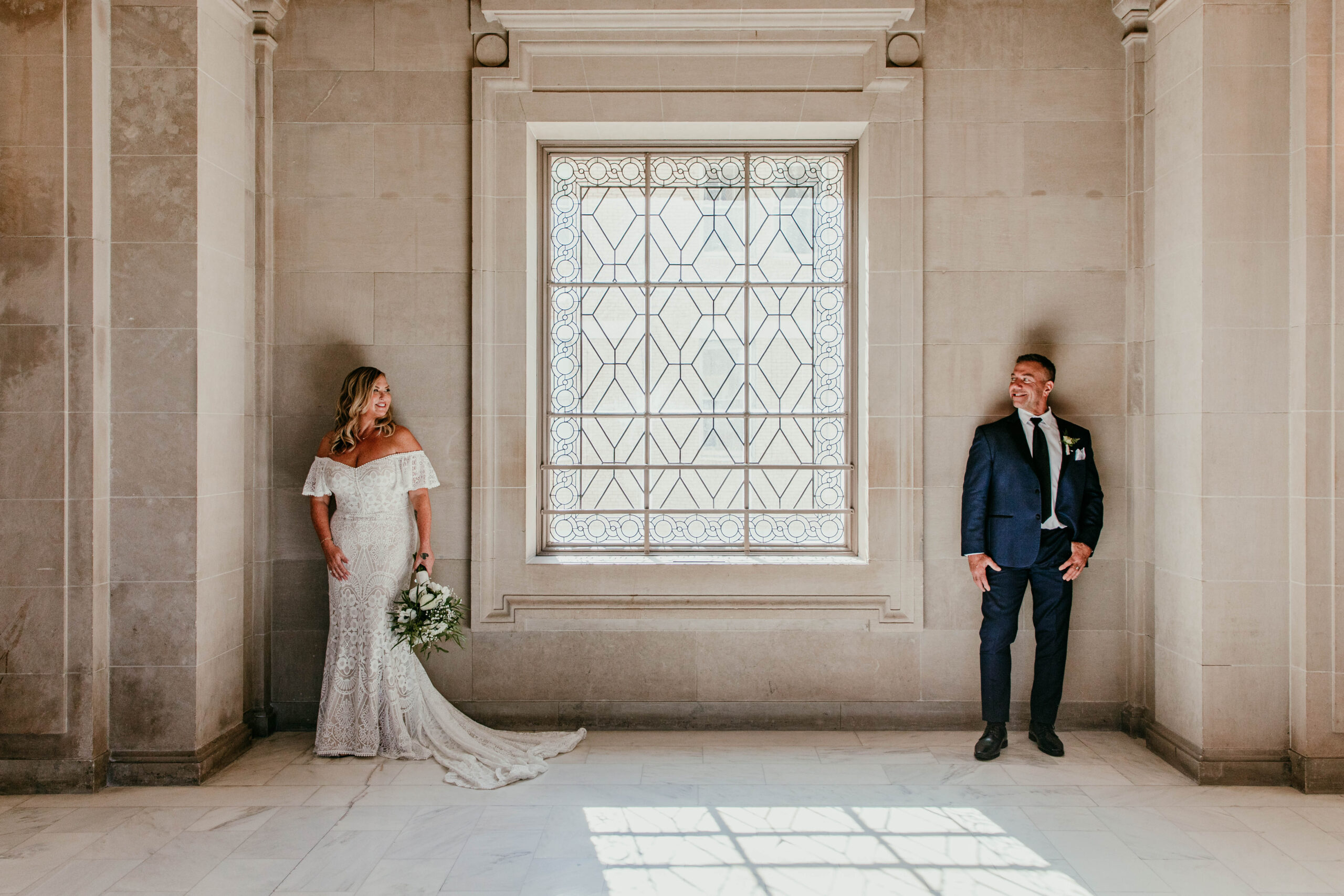 Bride and groom standing apart near the ornate window inside San Francisco City Hall during their elopement, captured by a san francisco elopement photographer.