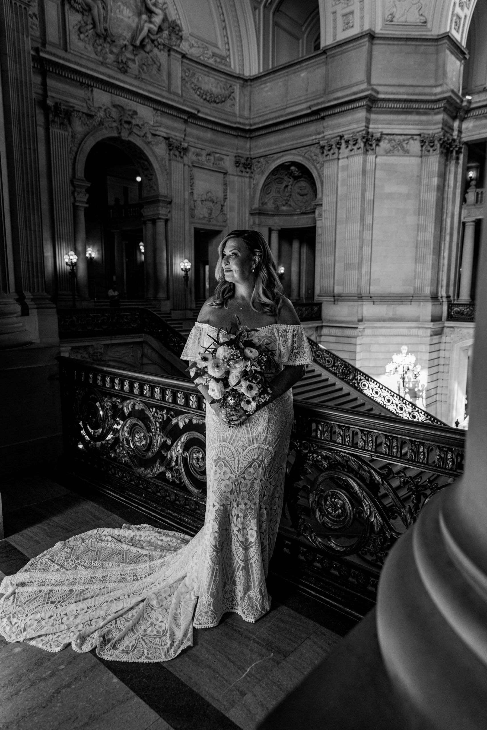 Black and white portrait of the bride holding her bouquet on the balcony inside San Francisco City Hall, captured by a san francisco elopement photographer.