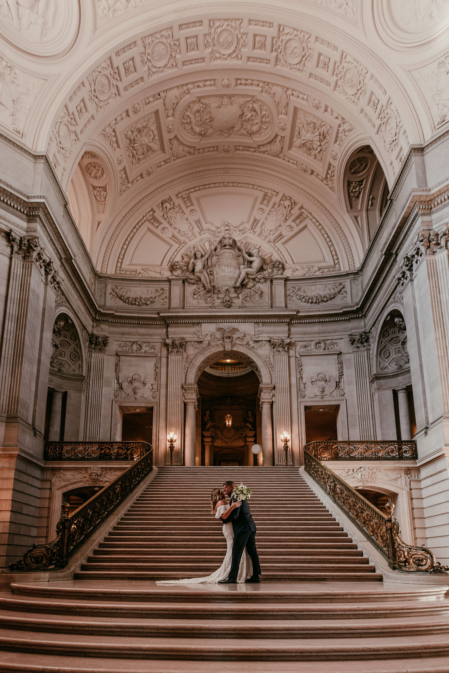 Bride and groom embracing on the Grand Staircase inside San Francisco City Hall, showcasing the architecture and romance of their elopement, captured by a san francisco elopement photographer.